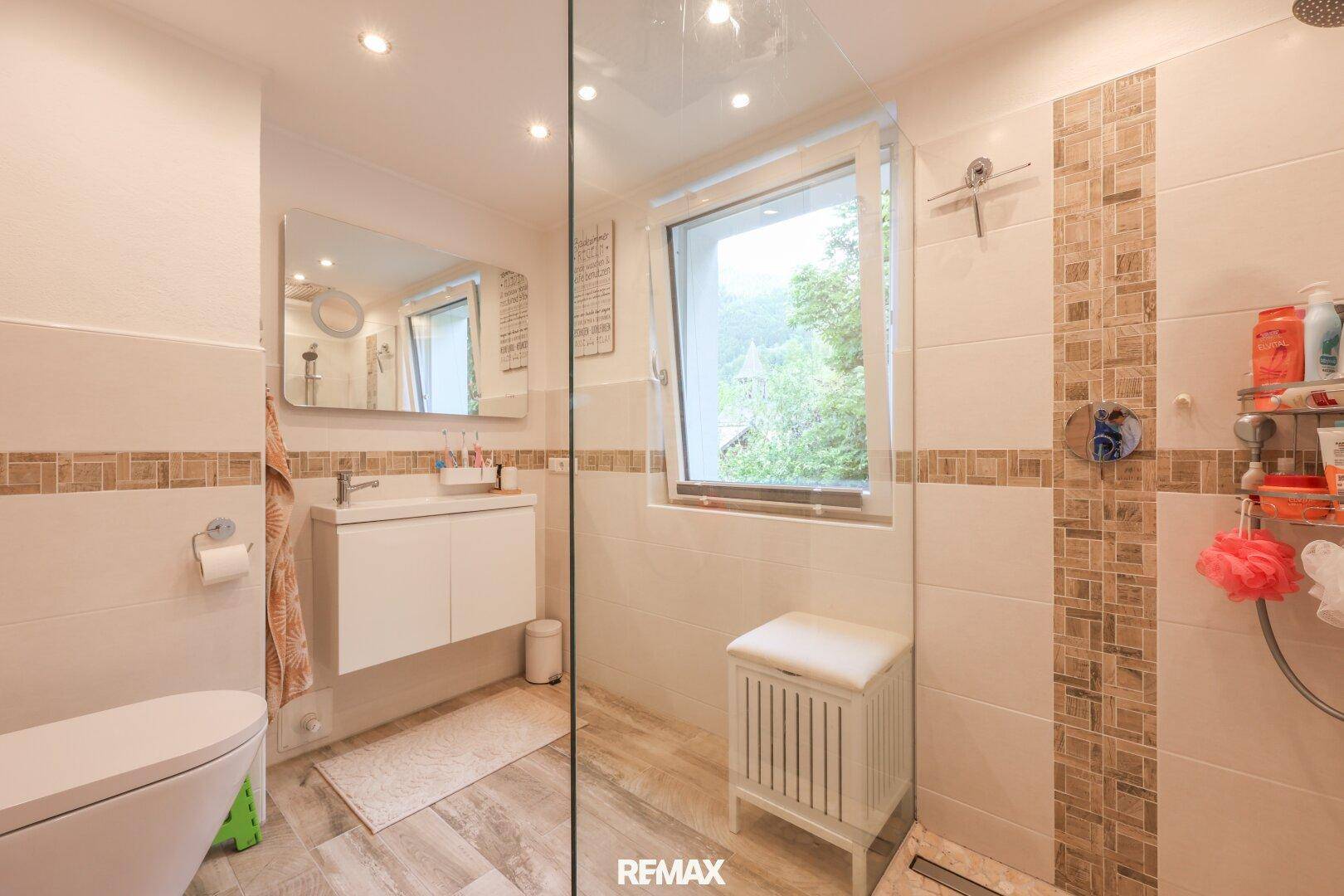 Modernes Badezimmer mit begehbarer Dusche, Wand-WC, Waschbecken und Fenster.