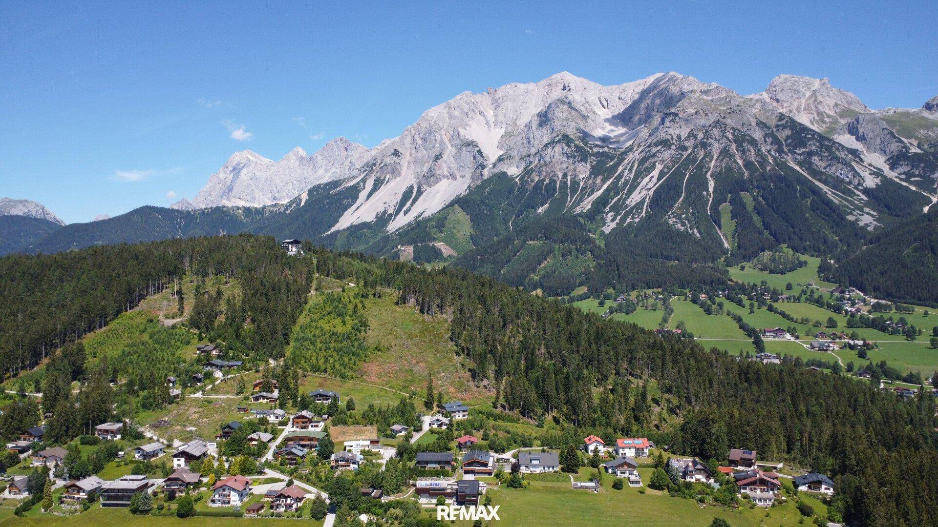 Panoramablick aus der Luft auf ein malerisches Dorf, umgeben von Wäldern und hohen Bergen.