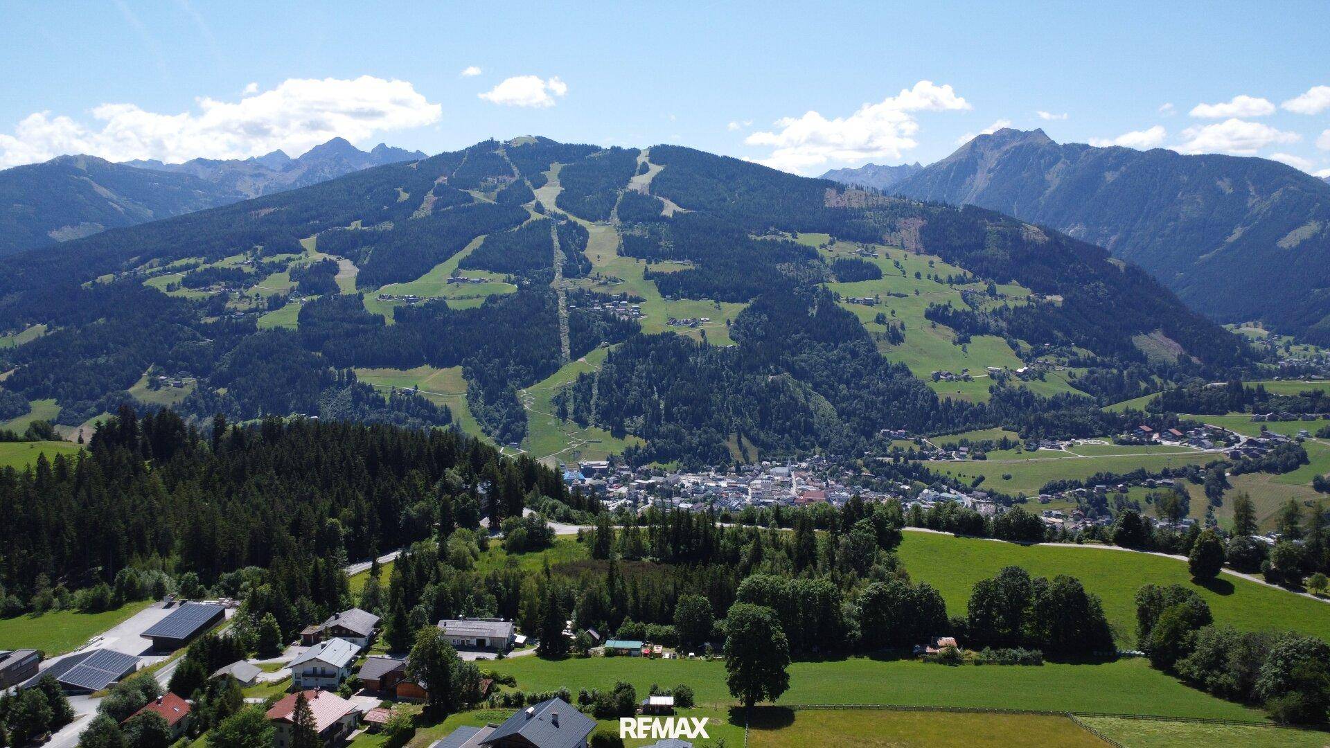 Weitläufige Luftaufnahme einer Stadt im Tal mit umliegenden Wäldern und Skipisten an den Bergen.