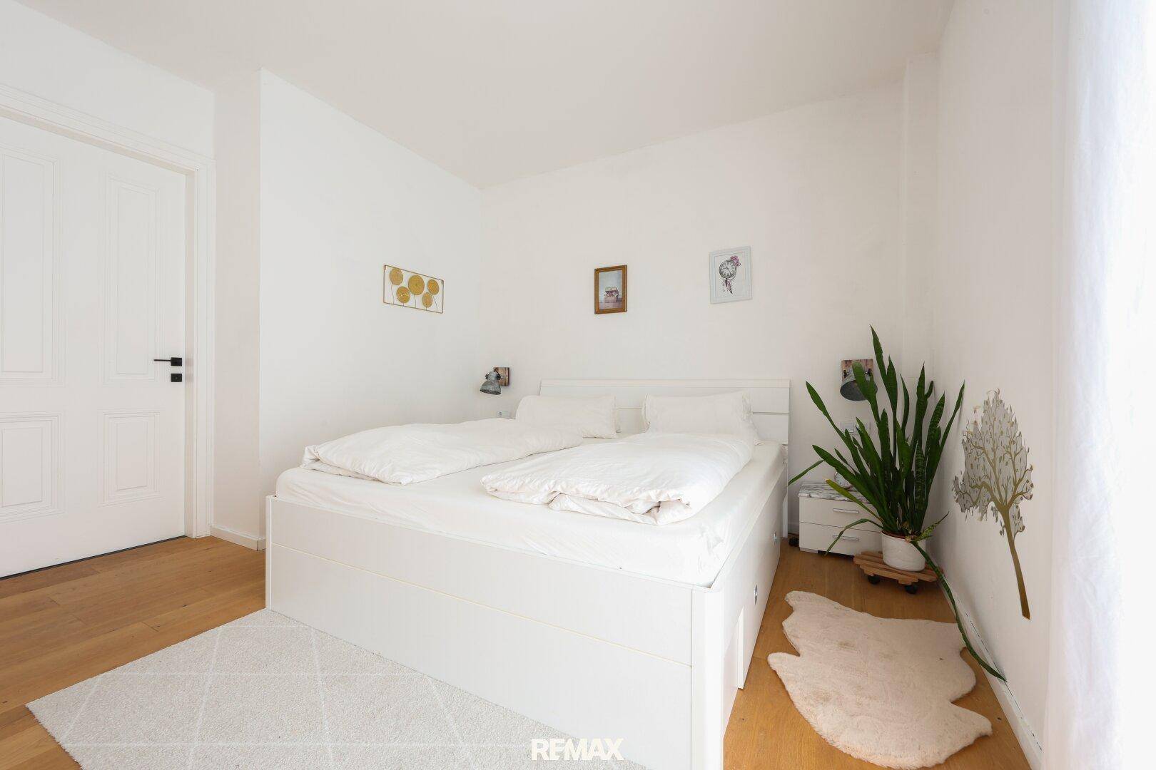 Helles Schlafzimmer mit weißem Bett, Holzboden und minimalistischer Dekoration.
