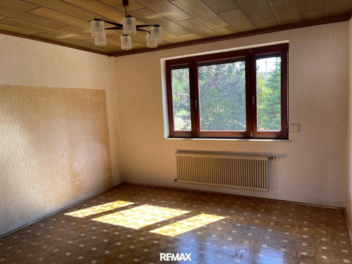Helles Zimmer mit Parkettboden, Holzdecke und Fenster mit Blick ins Grüne.