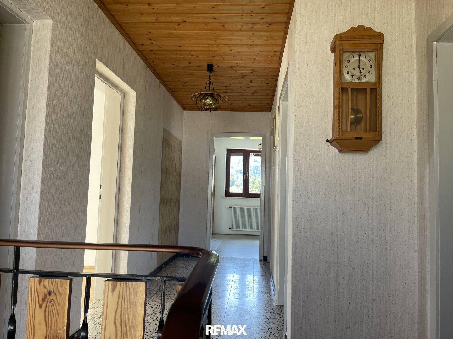 Flur mit Holzdecke, Terrazzoboden und traditioneller Wanduhr.