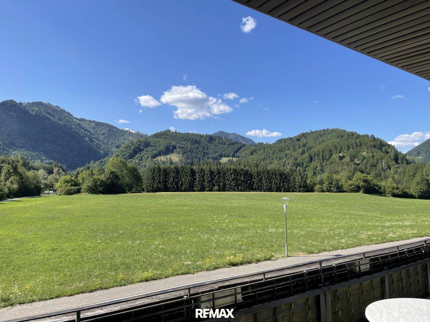 Weitläufiger Blick vom Balkon auf grüne Wiesen und bewaldete Berge.