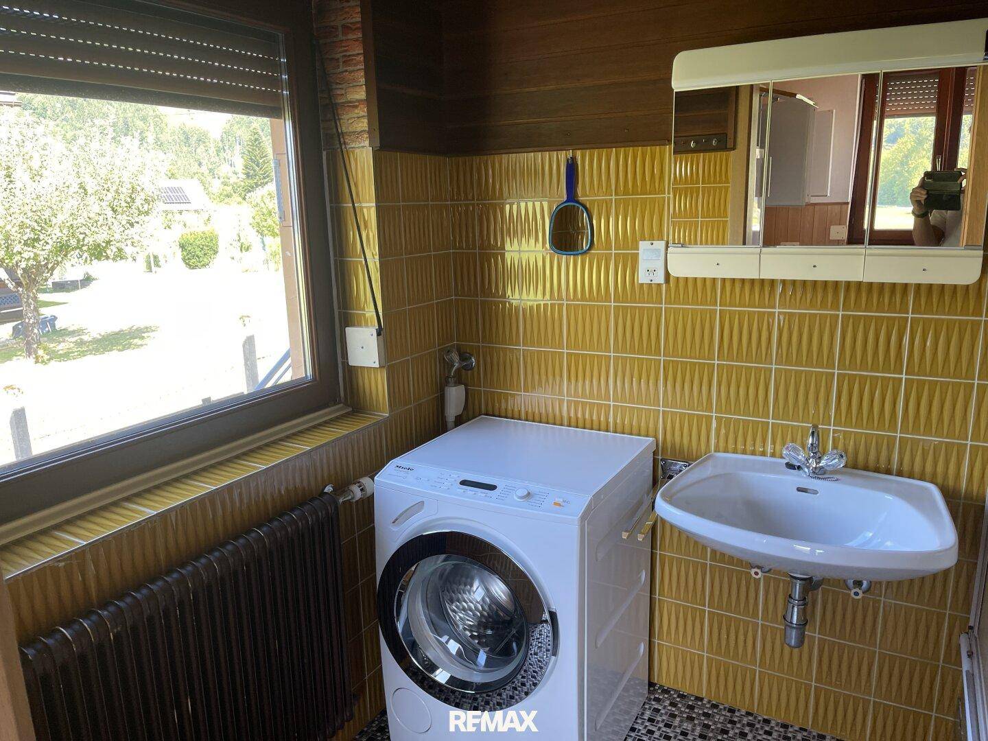 Badezimmer mit gelben Fliesen, Waschbecken und Waschmaschine, hell durch Fenster.