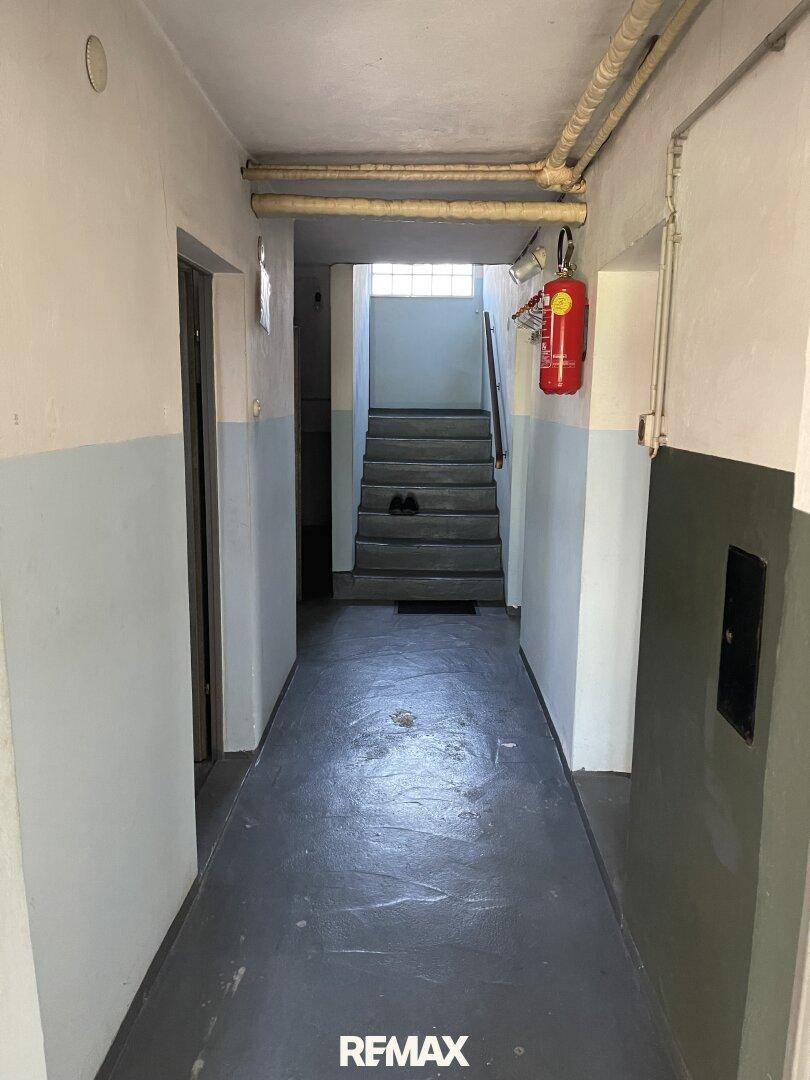 Kellerflur mit Betonboden und Treppe, die in die oberen Stockwerke führt.