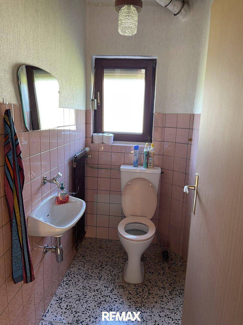 Kleines WC mit rosa Fliesen, Toilette und Waschbecken, mit Fenster.