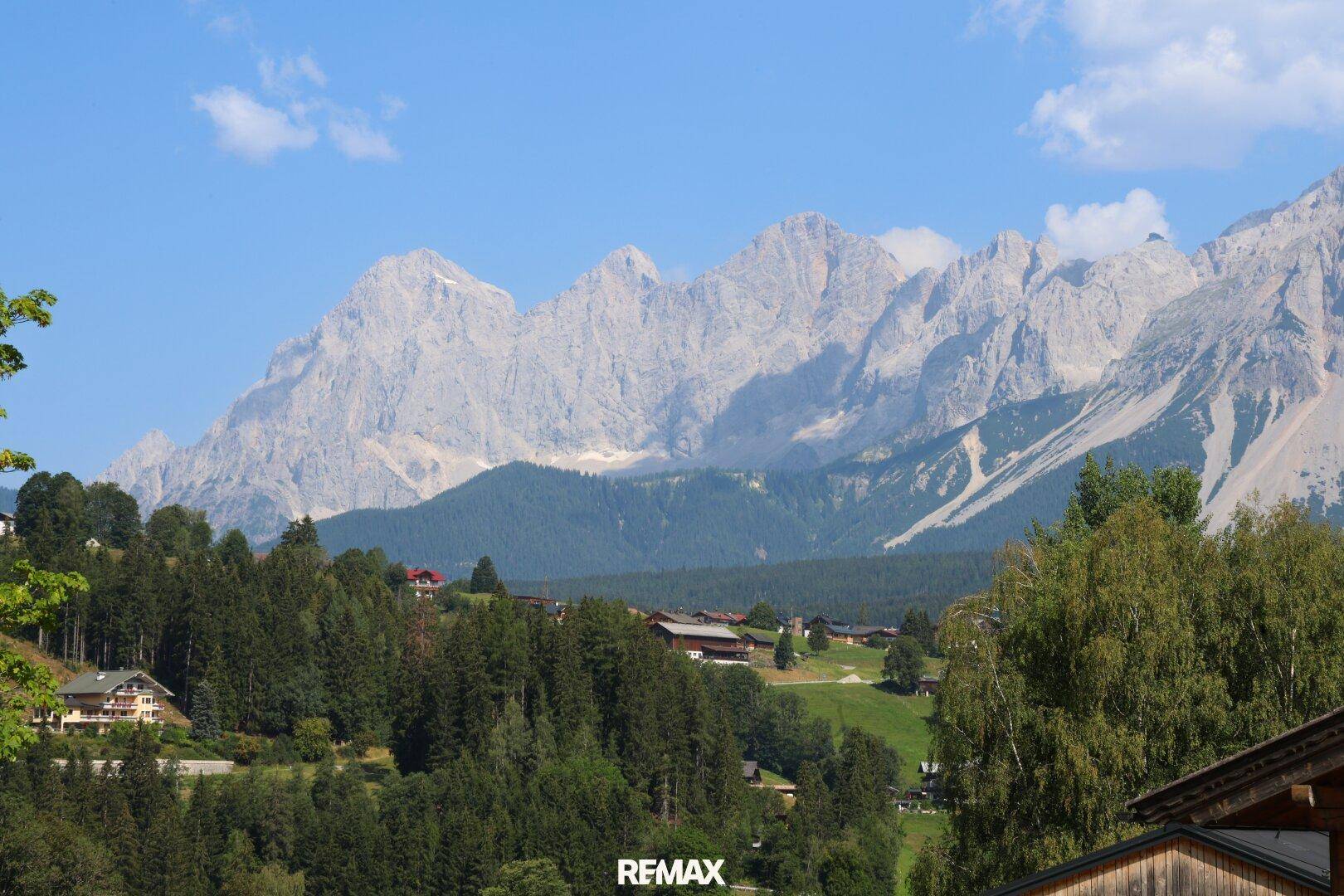 Eine beeindruckende Bergkette unter einem klaren blauen Himmel, umgeben von grünen Wäldern und Häusern.