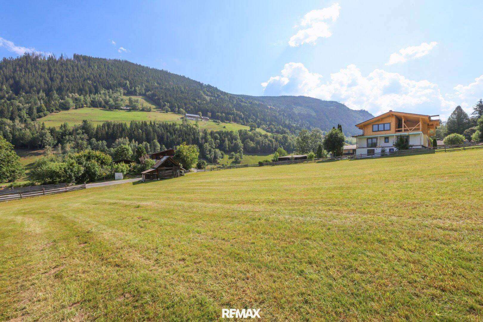 Ein modernes Haus mit Holzelementen und Balkon, umgeben von grünen Wiesen und Wäldern.