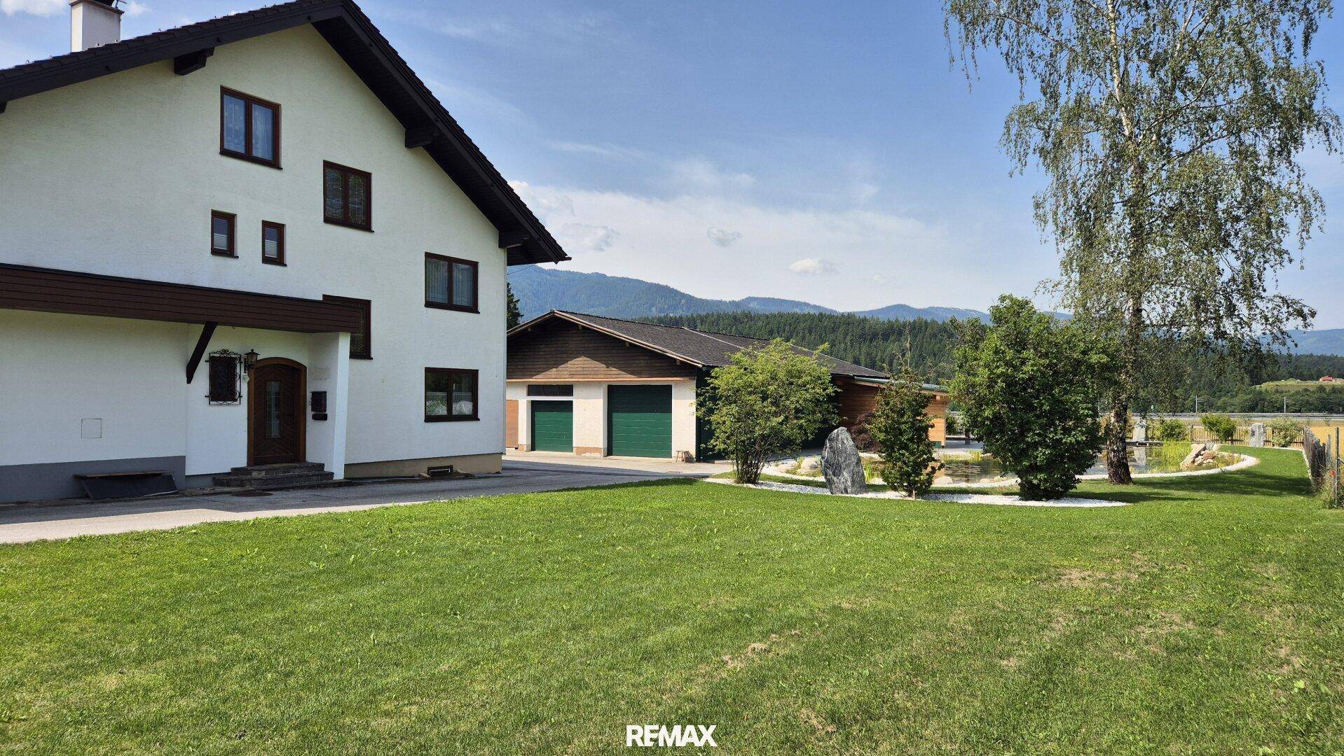 Haus mit großem Rasen und Nebengebäude im Hintergrund, umgeben von ländlicher Idylle.