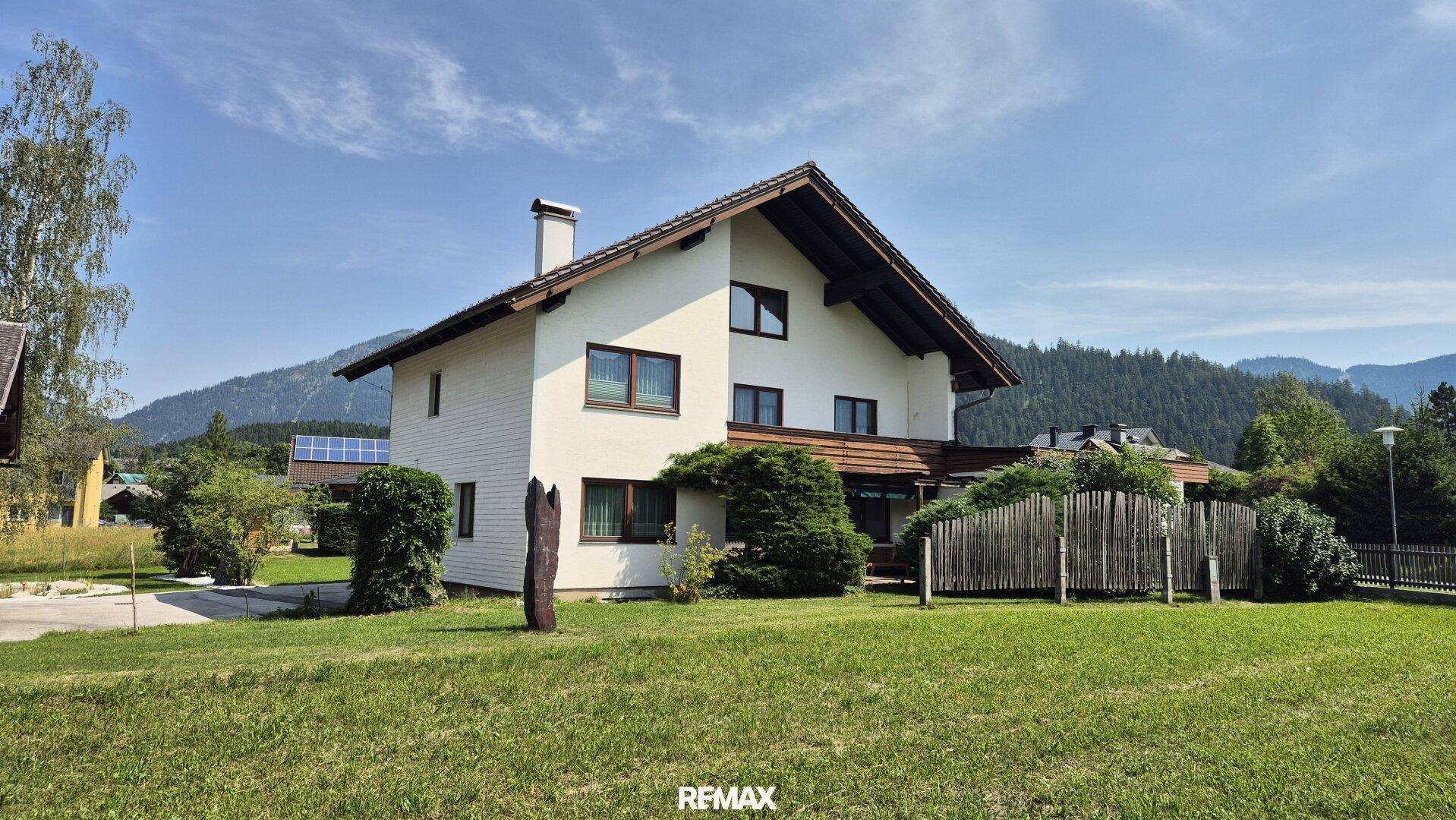 Weiß verputztes Haus mit braunem Satteldach und gepflegtem Gartenbereich in ländlicher Umgebung.