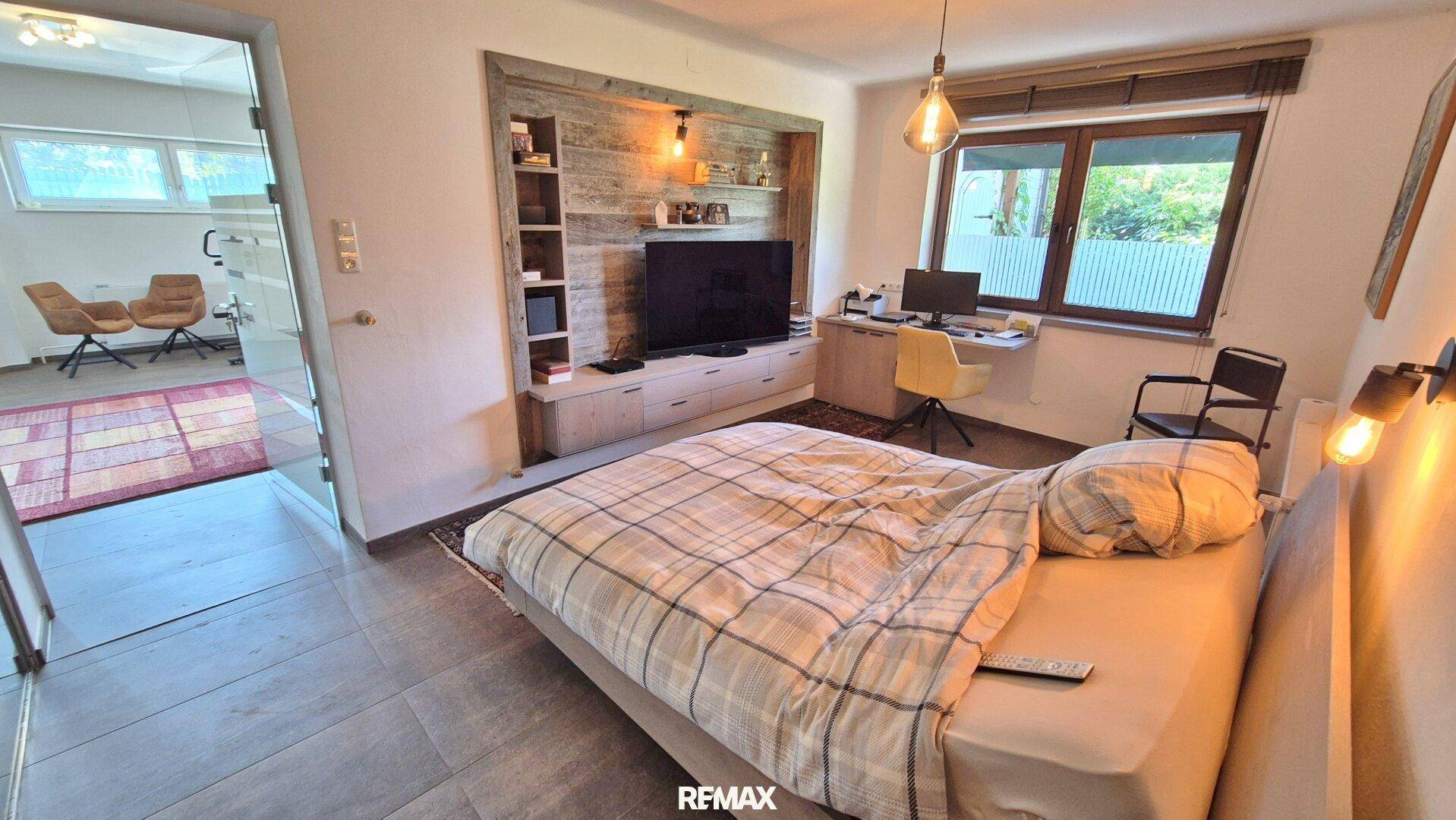 Gemütliches Schlafzimmer mit Doppelbett, integriertem TV-Bereich und Schreibtisch am Fenster.