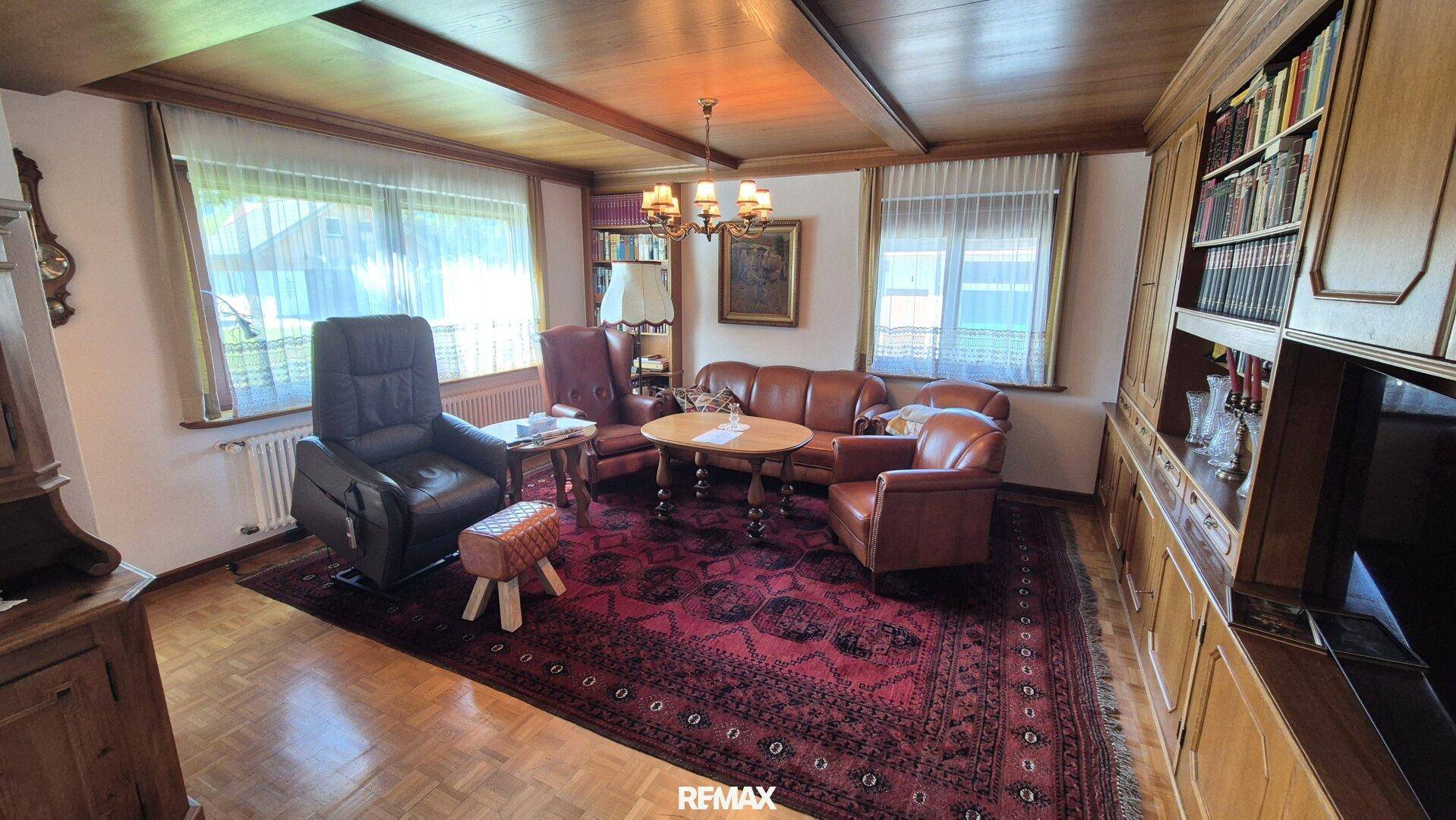 Traditionelles Wohnzimmer mit Holzbalkendecke, Ledersofas und großem Teppich.