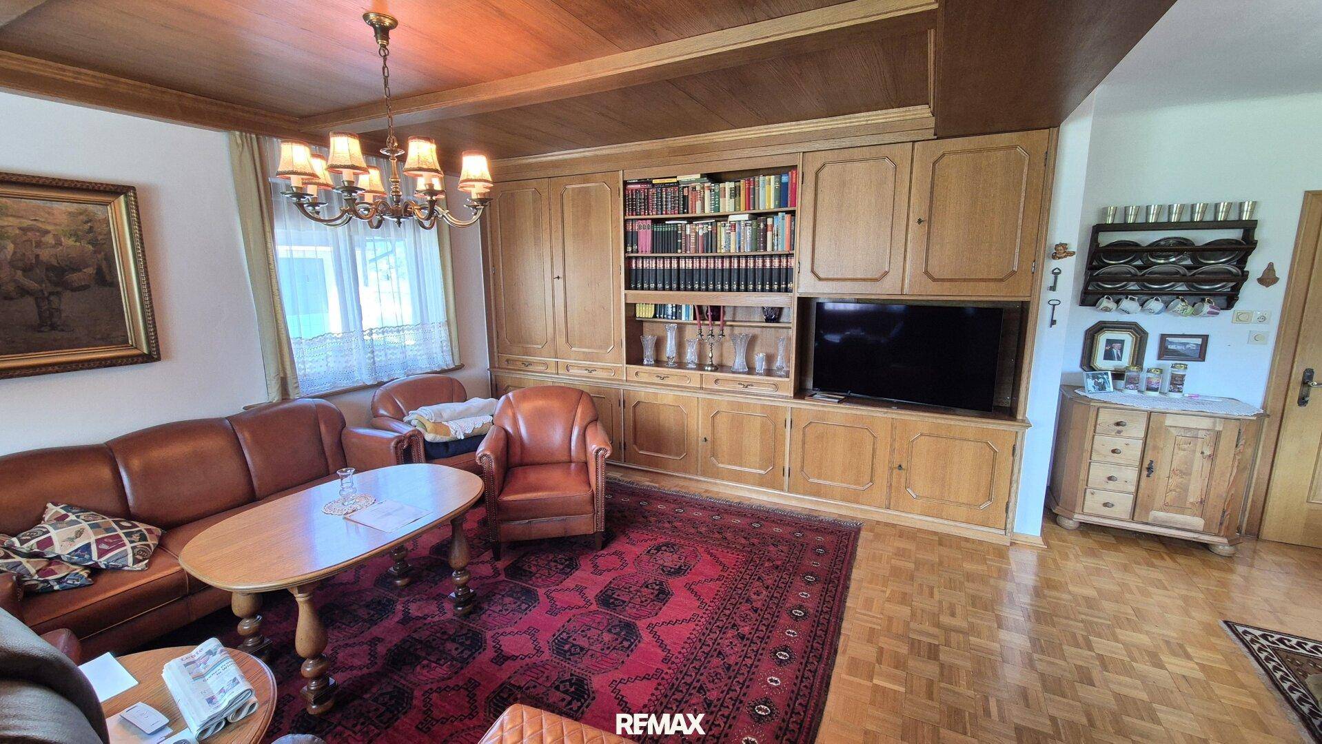 Gemütliches Wohnzimmer mit Holzeinbauten, Ledermöbeln und traditionellem Kronleuchter.