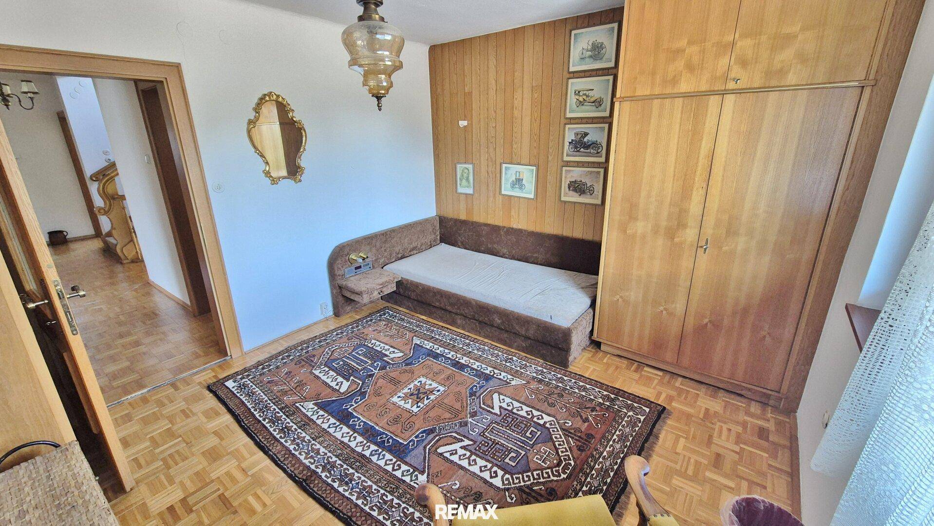 Schlafzimmer mit Holzwandverkleidung, Einzelbett, Kleiderschrank und traditionellem Teppich.
