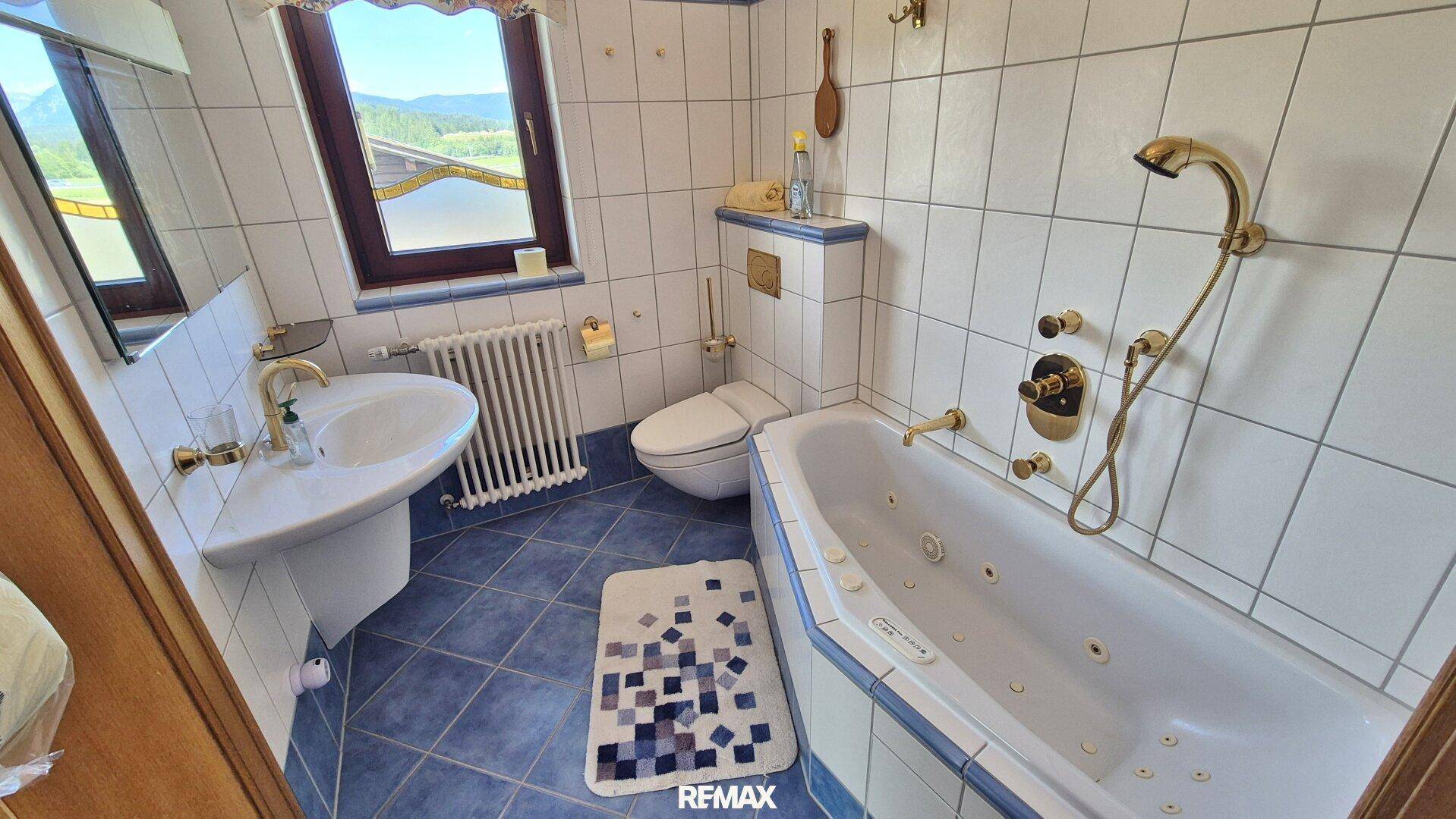 Traditionelles Badezimmer mit Eckbadewanne, WC, Waschbecken und Fenster mit Bergblick.