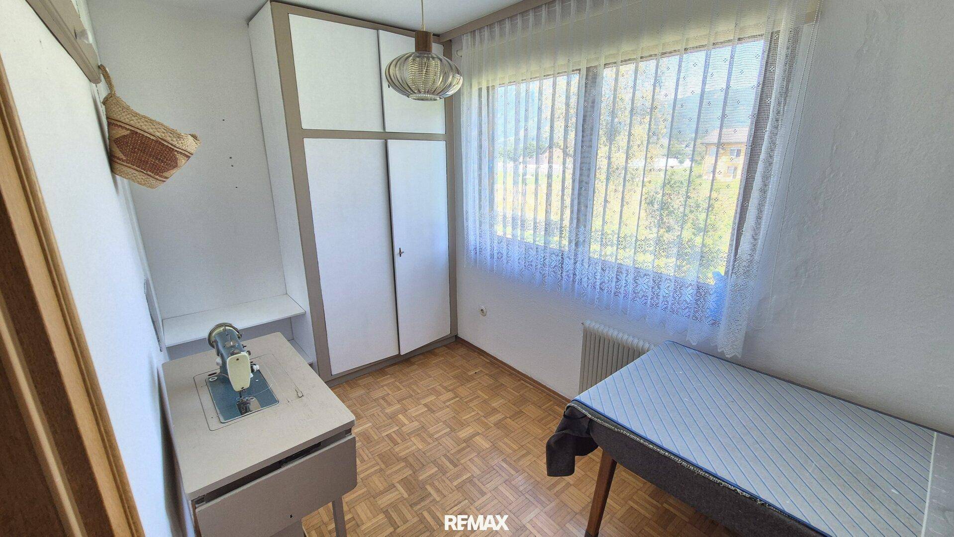 Kleines Zimmer mit großem Fenster, Kleiderschrank und Nähmaschine, ideal als Gästezimmer.