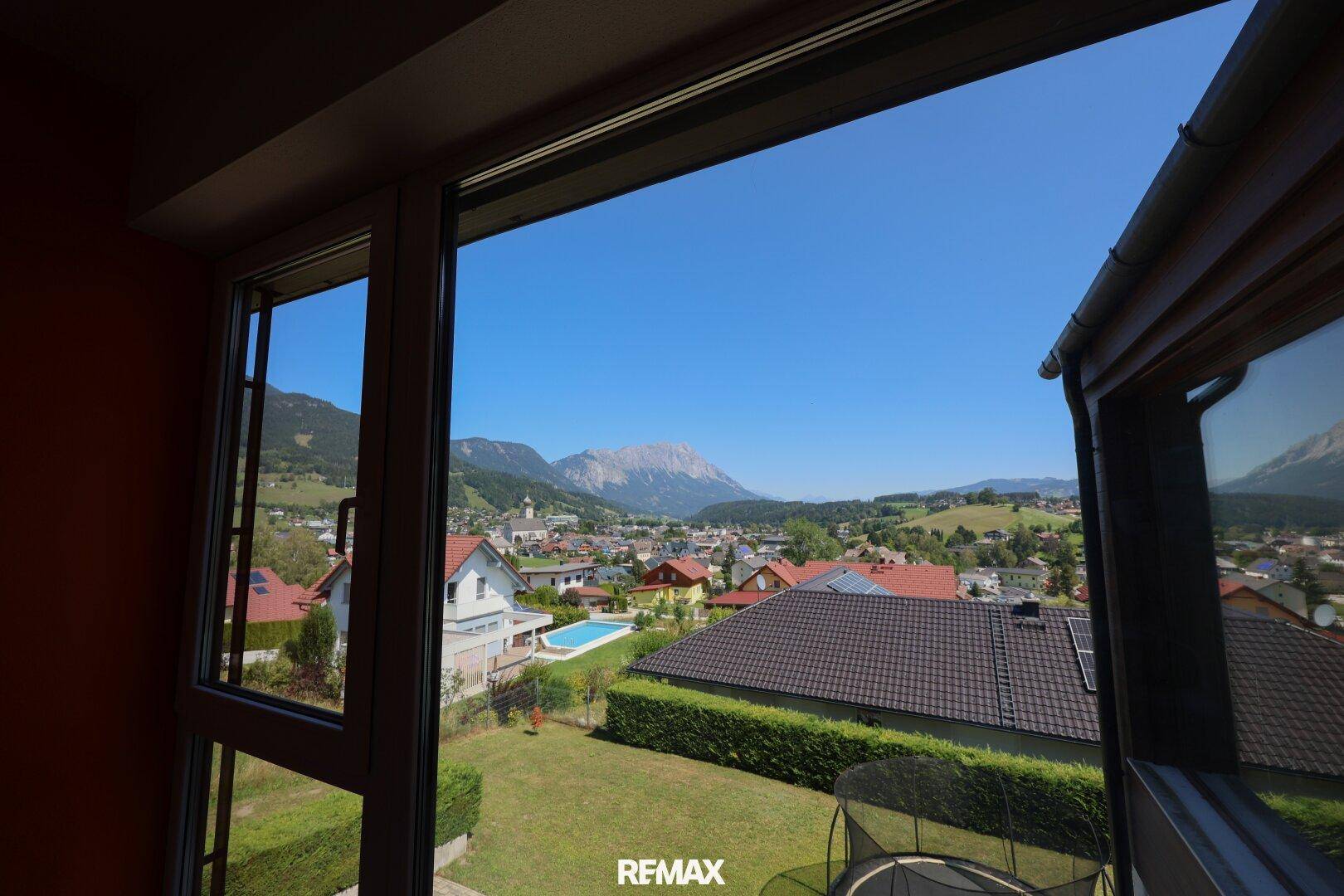 Panoramablick aus dem Fenster auf die Stadt, Berge und einen Pool.