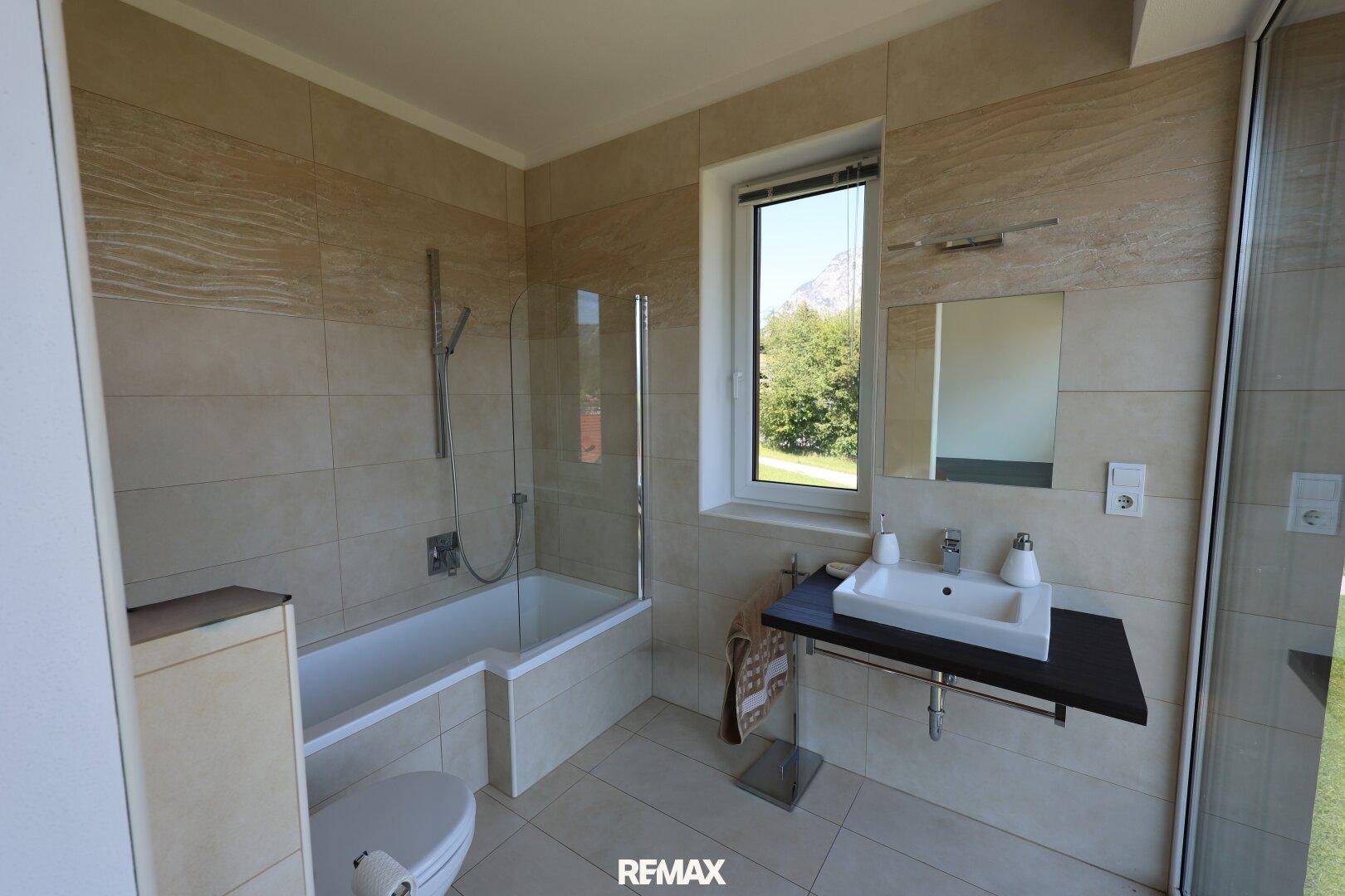 Modernes Badezimmer mit Badewanne, Waschbecken und hellen Fliesen.