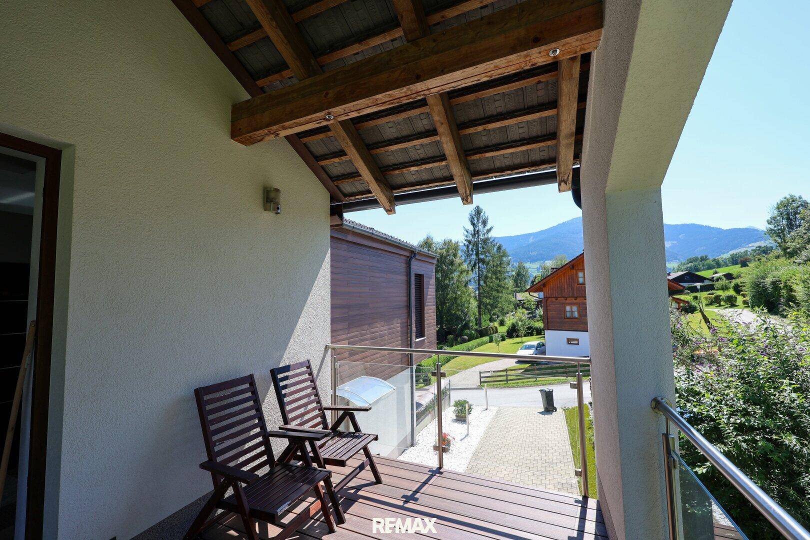 Überdachter Balkon mit Holzmöbeln und Blick auf die grüne Umgebung.