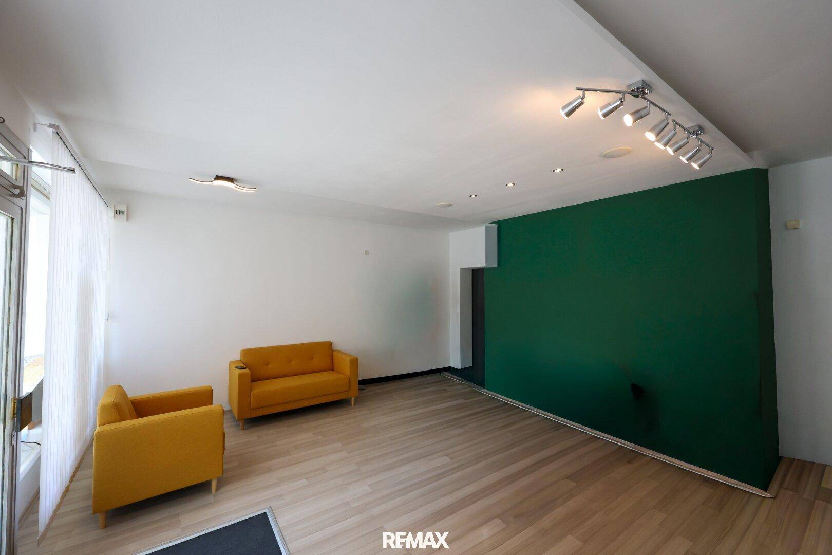 Heller Büroraum mit Holzboden, einer grünen Akzentwand und modernen gelben Sofas.
