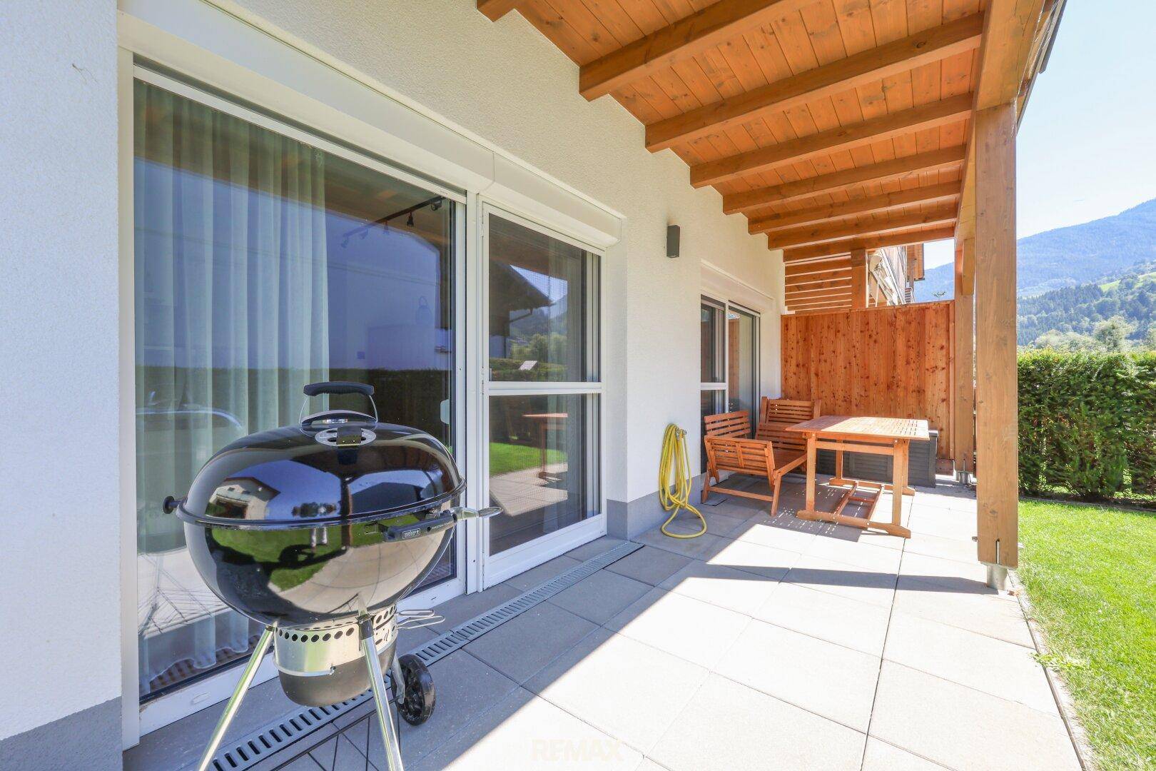 Sonniger Terrassenbereich mit Grill und Gartenmöbeln, ideal für Mahlzeiten im Freien.