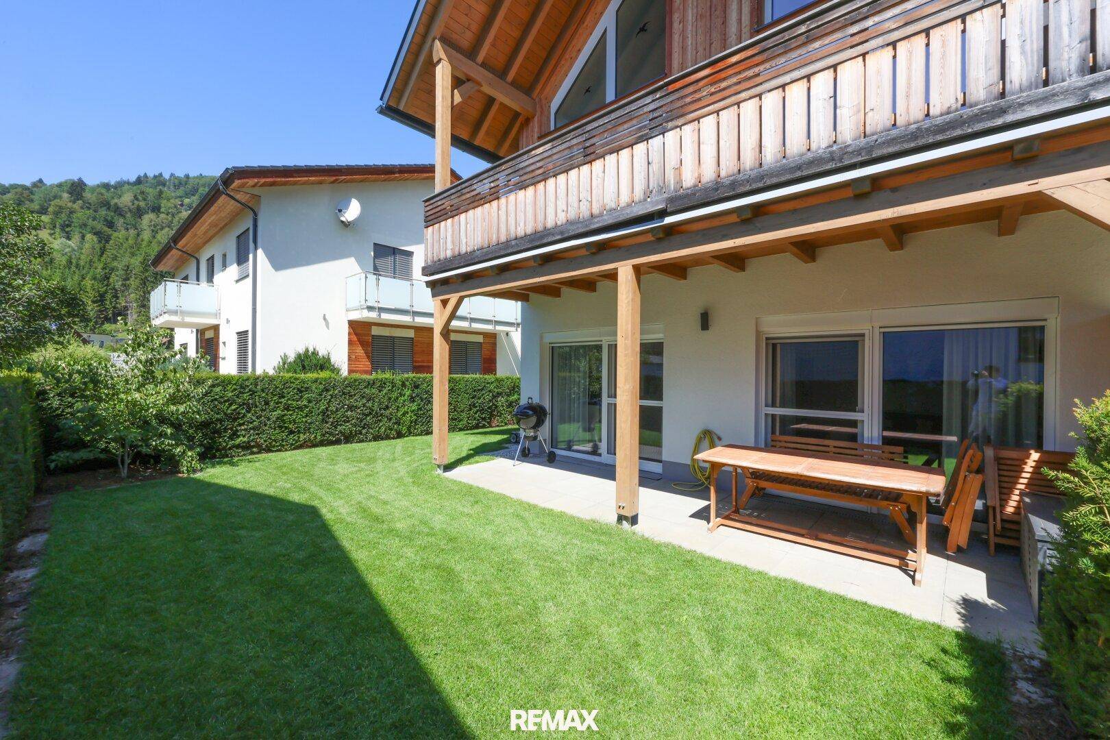Gepflegter Rasenbereich mit Terrasse und Hecke, umgeben von grüner Landschaft.