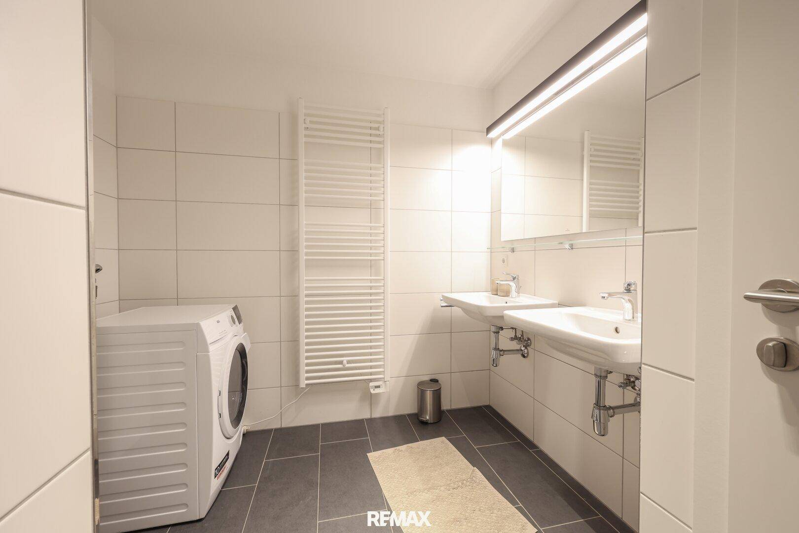 Modernes Badezimmer mit Doppelwaschbecken, Fliesenboden und Handtuchheizkörper.