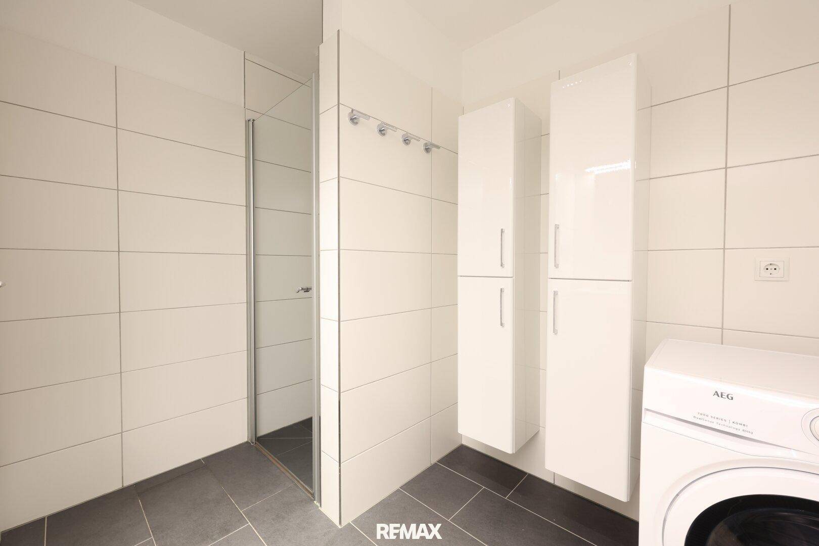 Helles Badezimmer mit Duschkabine, weißen Schränken und Waschmaschine.