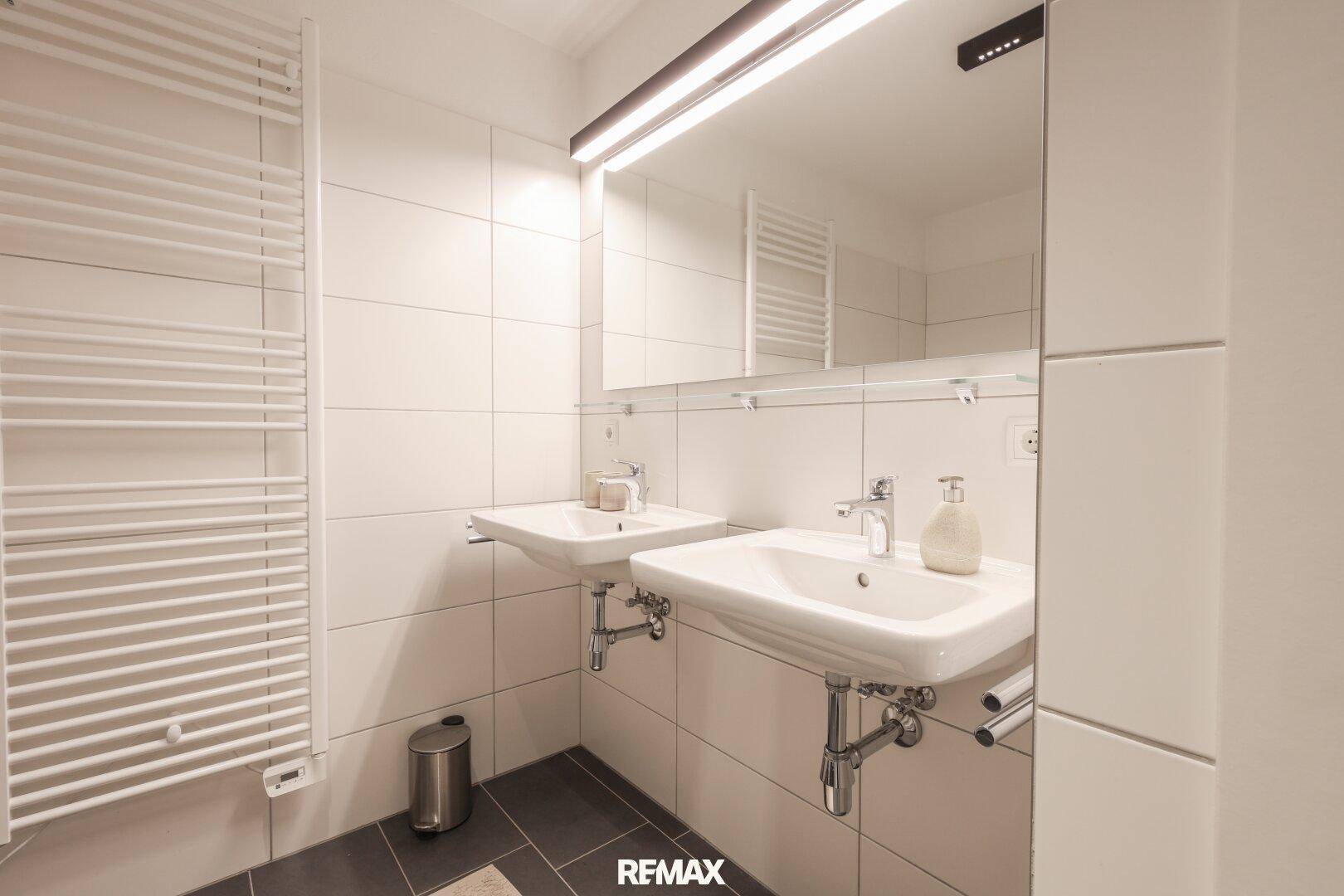 Modernes Badezimmer mit Doppelwaschbecken, großem Spiegel und Handtuchheizkörper.