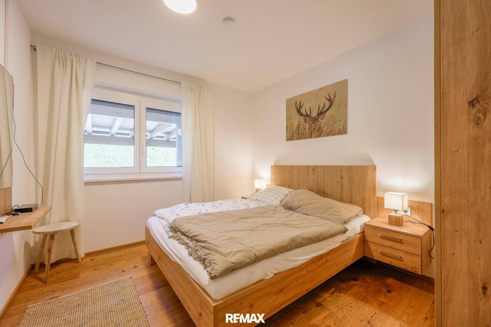 Helles Schlafzimmer mit Holzbett, Nachttischen und Fenster mit Blick ins Grüne.