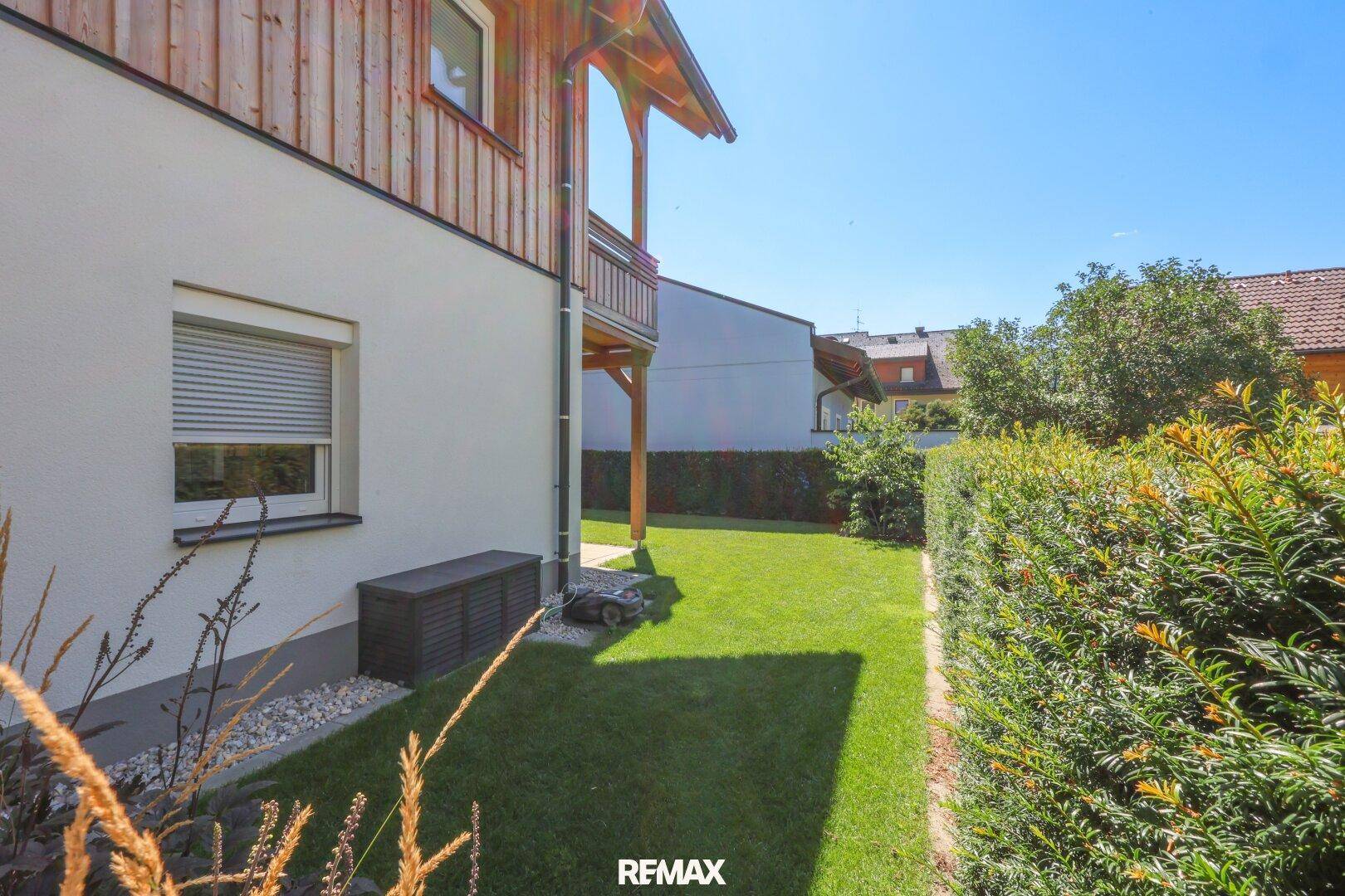 Seitlicher Gartenbereich mit Rasen, Hecke und einem kleinen Geräteschuppen.