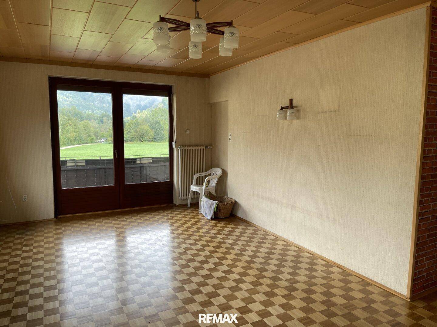 Helles Wohnzimmer mit Parkettboden, Holzdecke und Zugang zu einem Balkon mit Landschaftsblick.