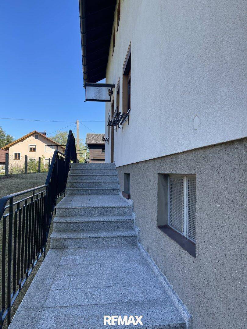 Außentreppe aus Granit führt zum Eingang des Hauses mit kleineren Fenstern im unteren Bereich.