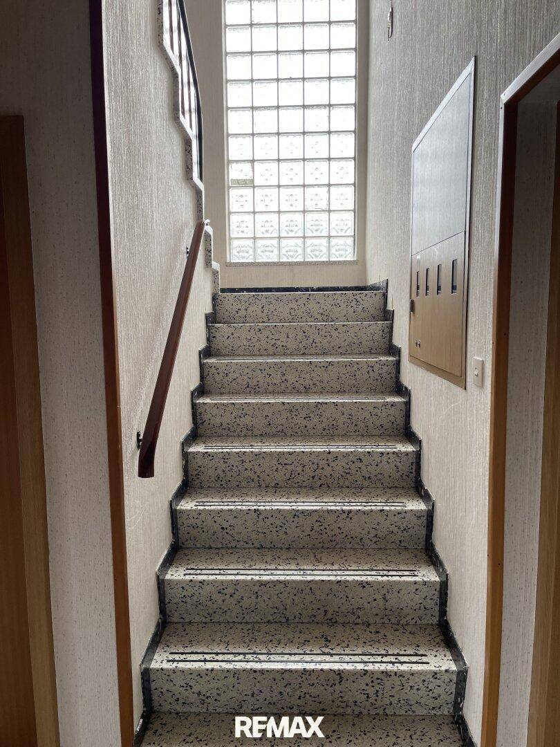 Treppenhaus mit Terrazzoboden und Glasbausteinfenster, das natürliches Licht spendet.
