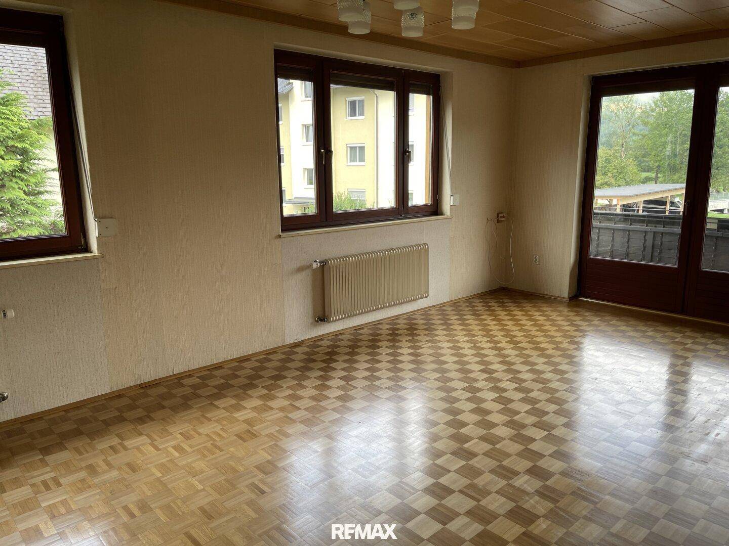 Geräumiges Wohnzimmer mit Parkettboden, Holzdecke und Blick auf die Umgebung durch große Fenster.