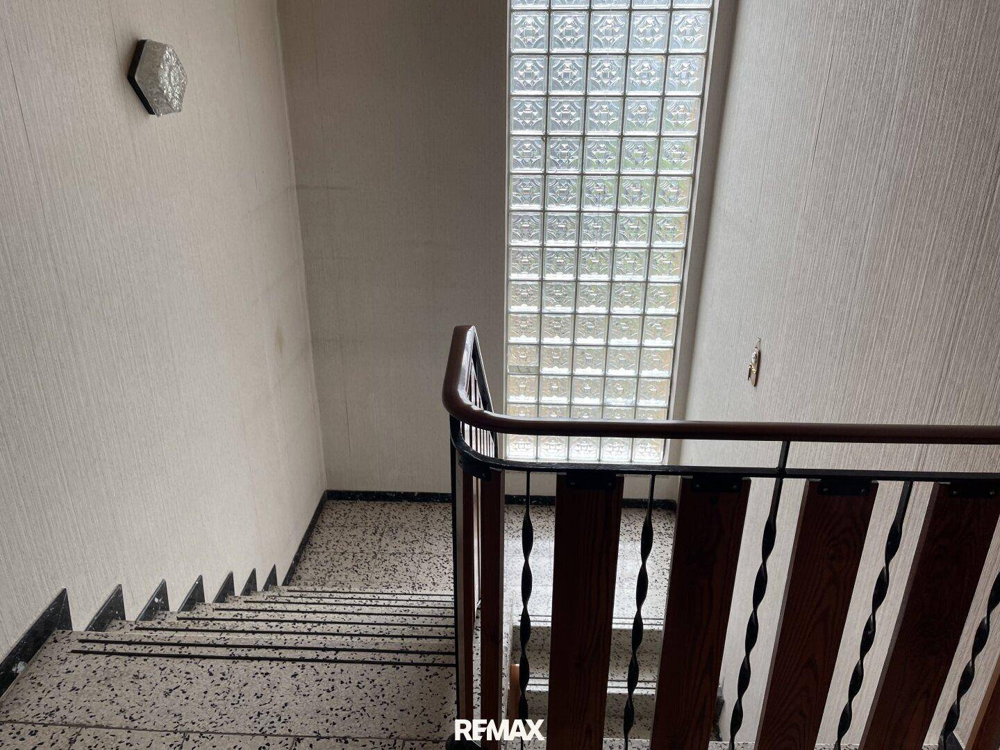 Treppenhaus mit Terrazzostufen und einem hohen Glasbausteinfenster für Tageslicht.