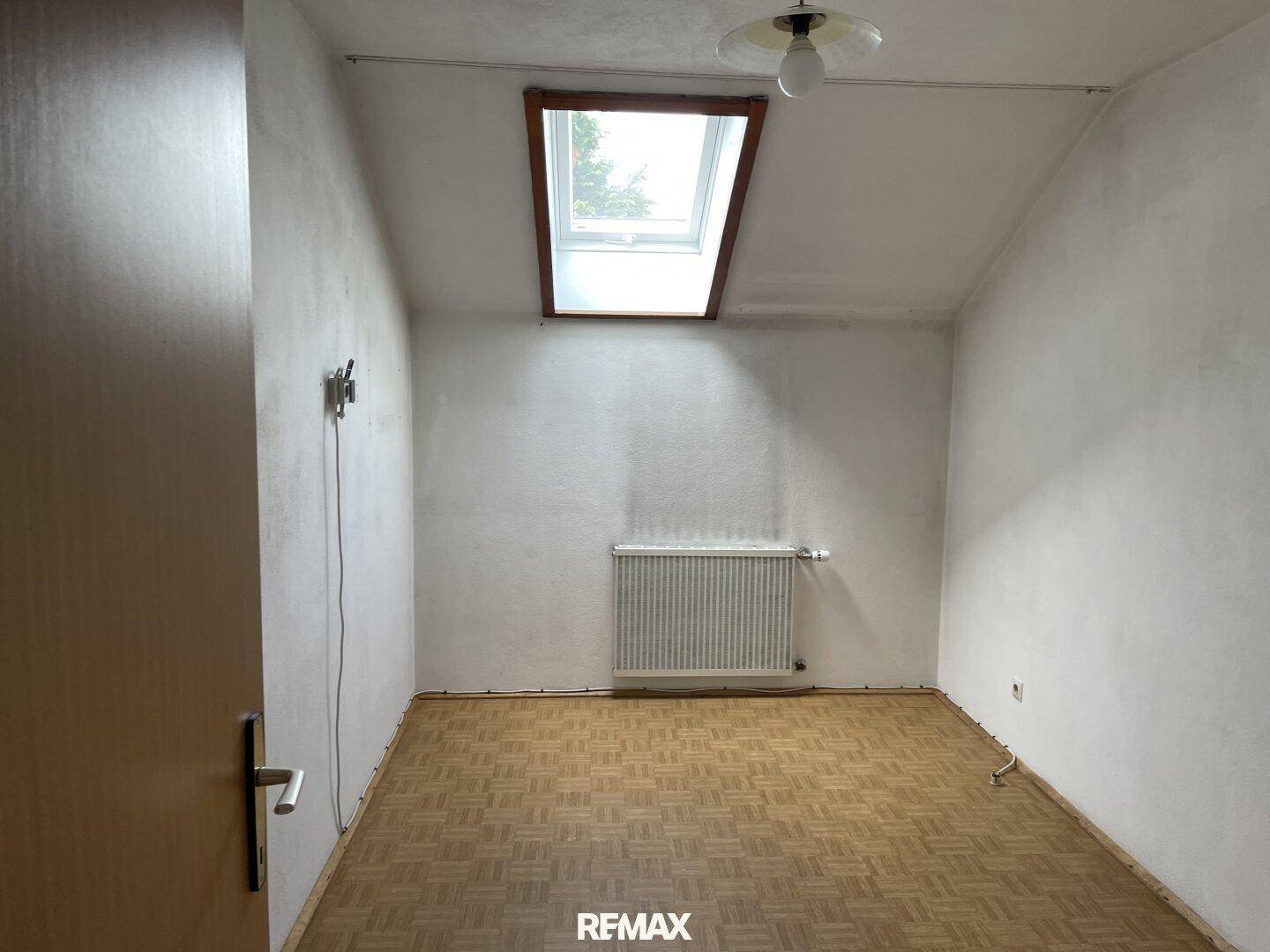 Dachzimmer mit Parkettboden, Dachschräge und einem Dachfenster für natürliches Licht.