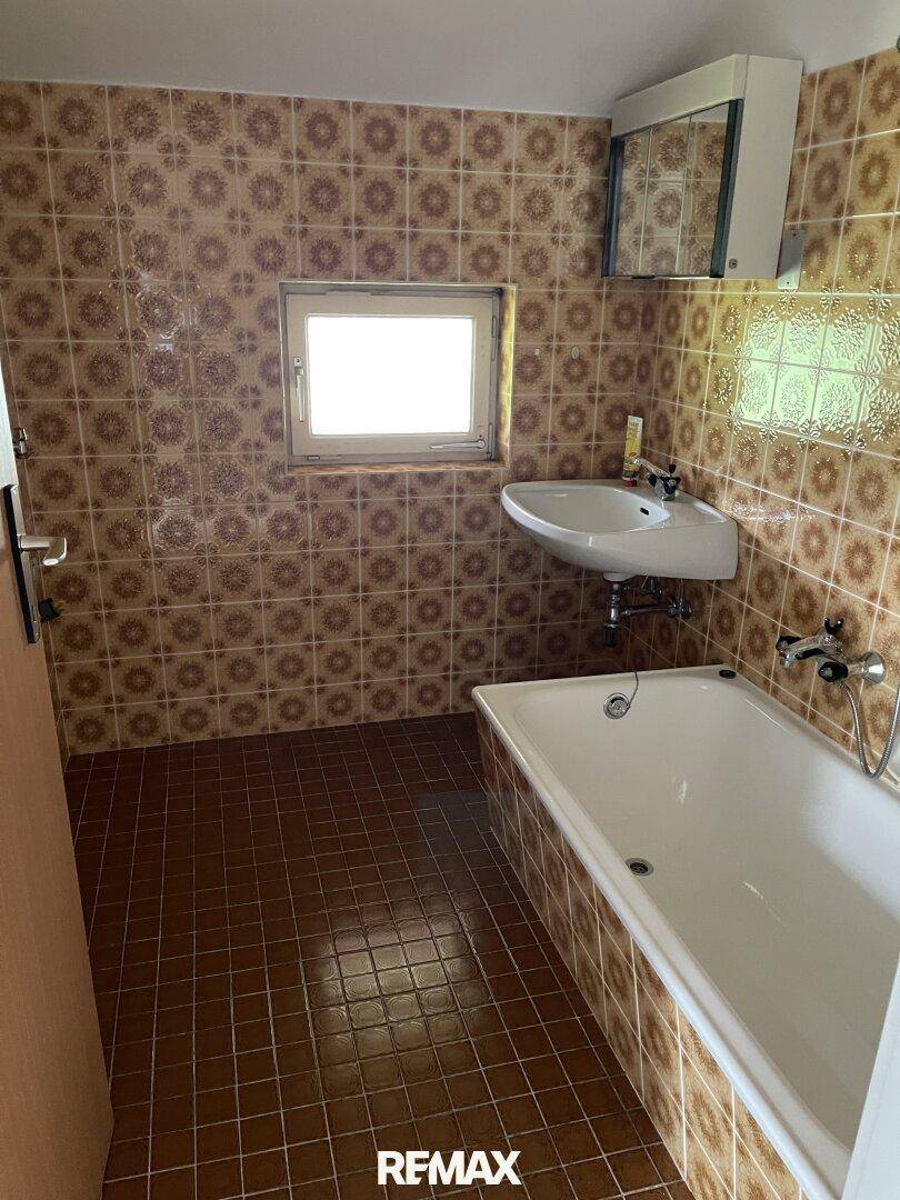 Badezimmer mit braunen Fliesen, Badewanne, Waschbecken und einem kleinen Fenster.
