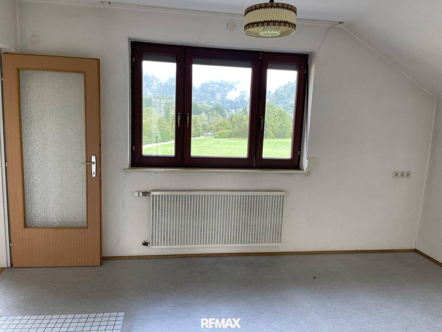 Schlafzimmer mit Teppichboden, Dachschräge und großem Fenster mit Blick ins Grüne.
