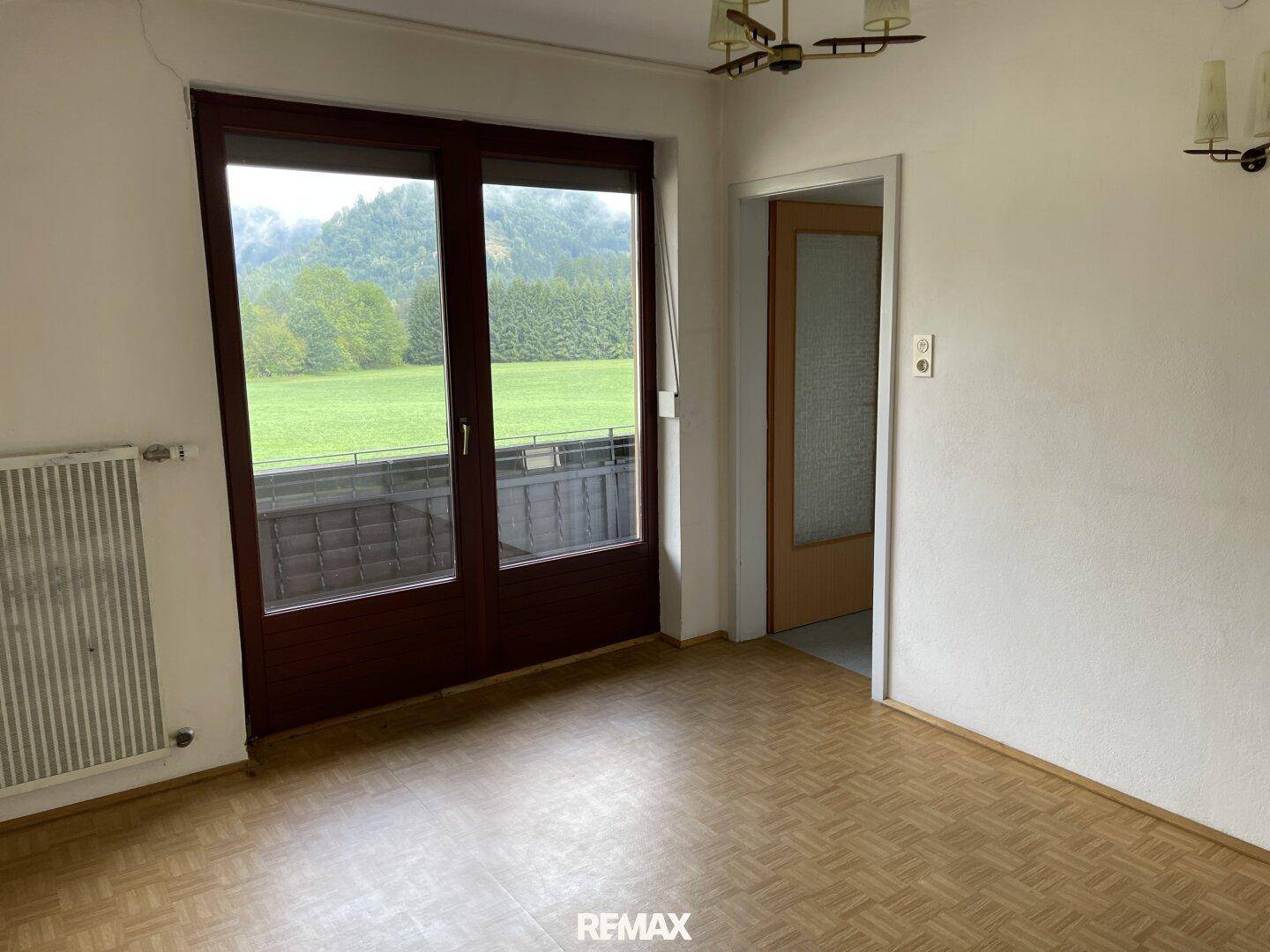 Wohnzimmer mit Parkettboden und Zugang zu einem Balkon, bietet einen weiten Blick.