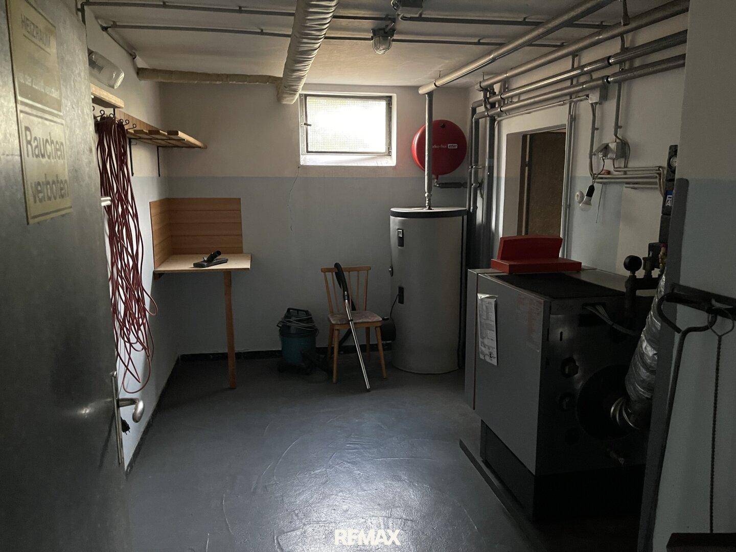Funktionaler Kellerraum mit Heizungsanlage, Warmwasserspeicher und sichtbaren Rohren an der Decke.