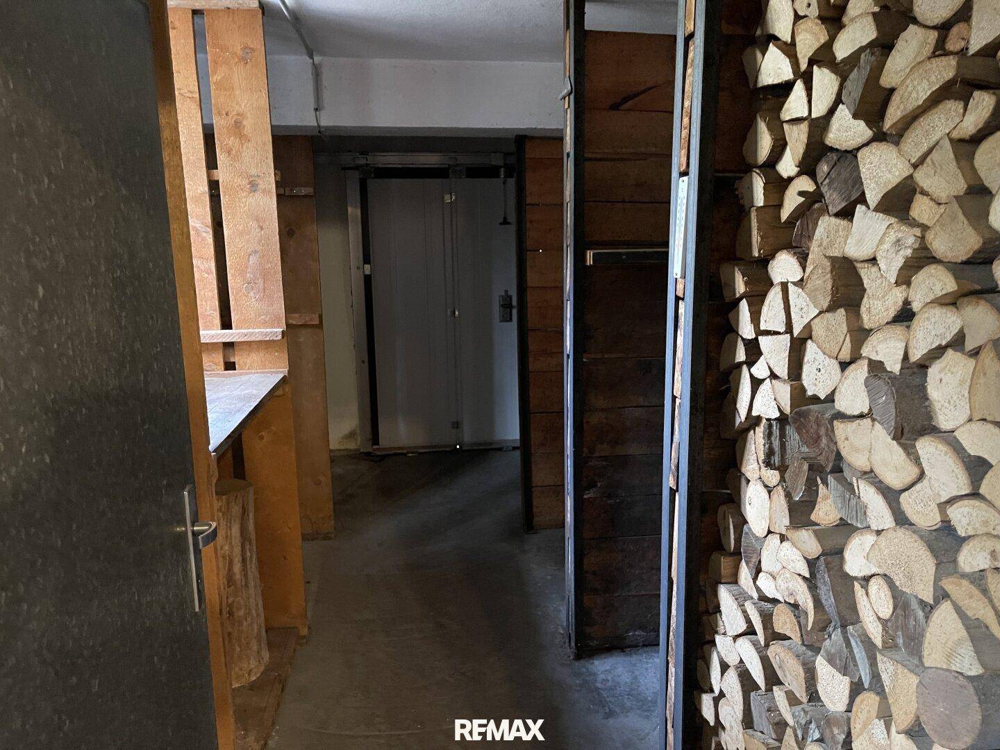 Kellerraum mit großem Holzstapel zur Lagerung von Brennholz und Zugang zu weiteren Bereichen.
