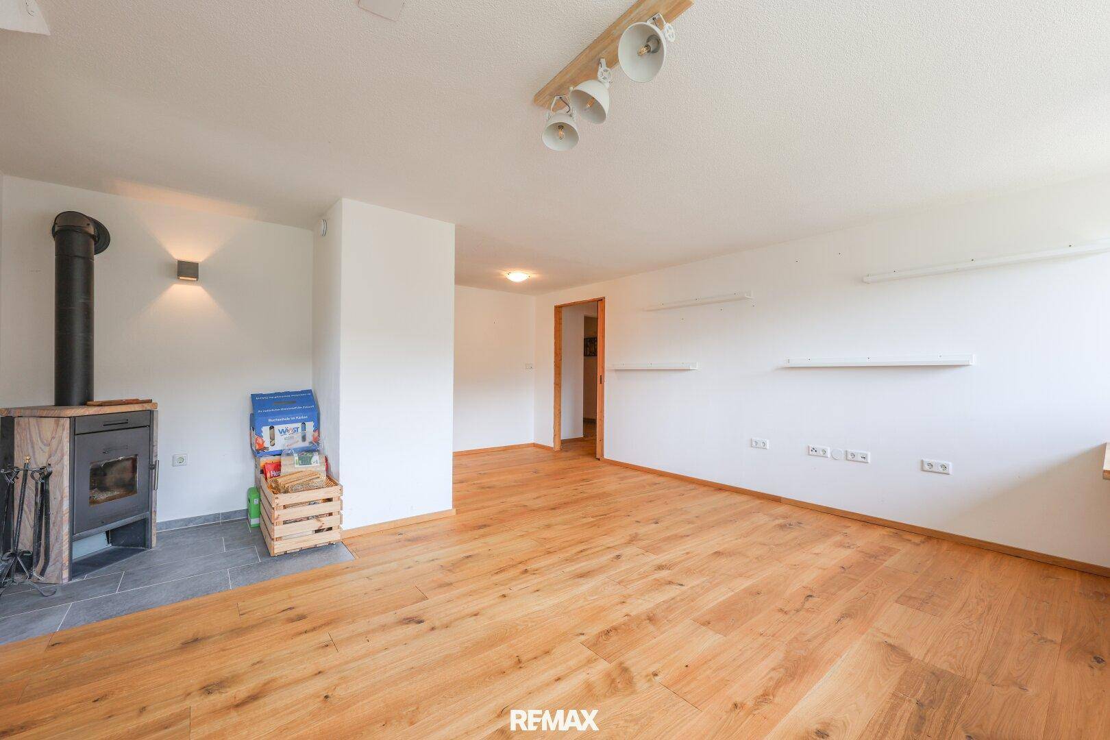 Gemütliches Wohnzimmer mit Holzboden, Kaminofen und Zugang zu einem Außenbereich.
