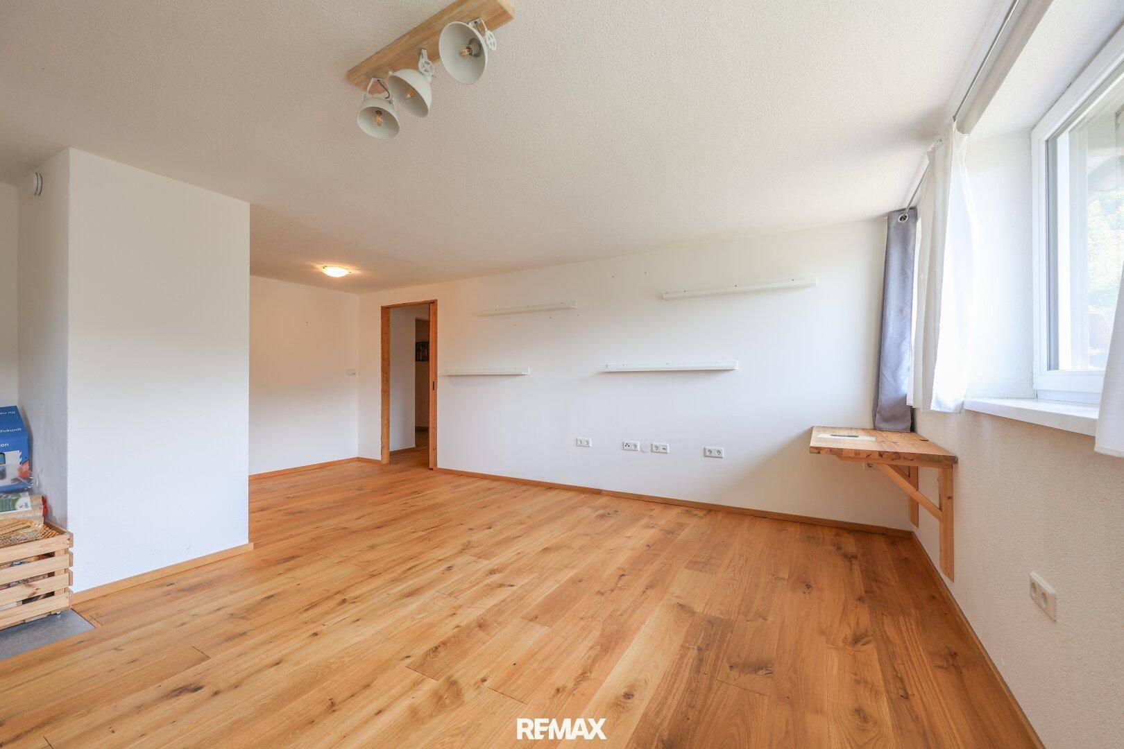 Geräumiges Wohnzimmer mit Holzboden, weißen Wänden und natürlichem Lichteinfall.