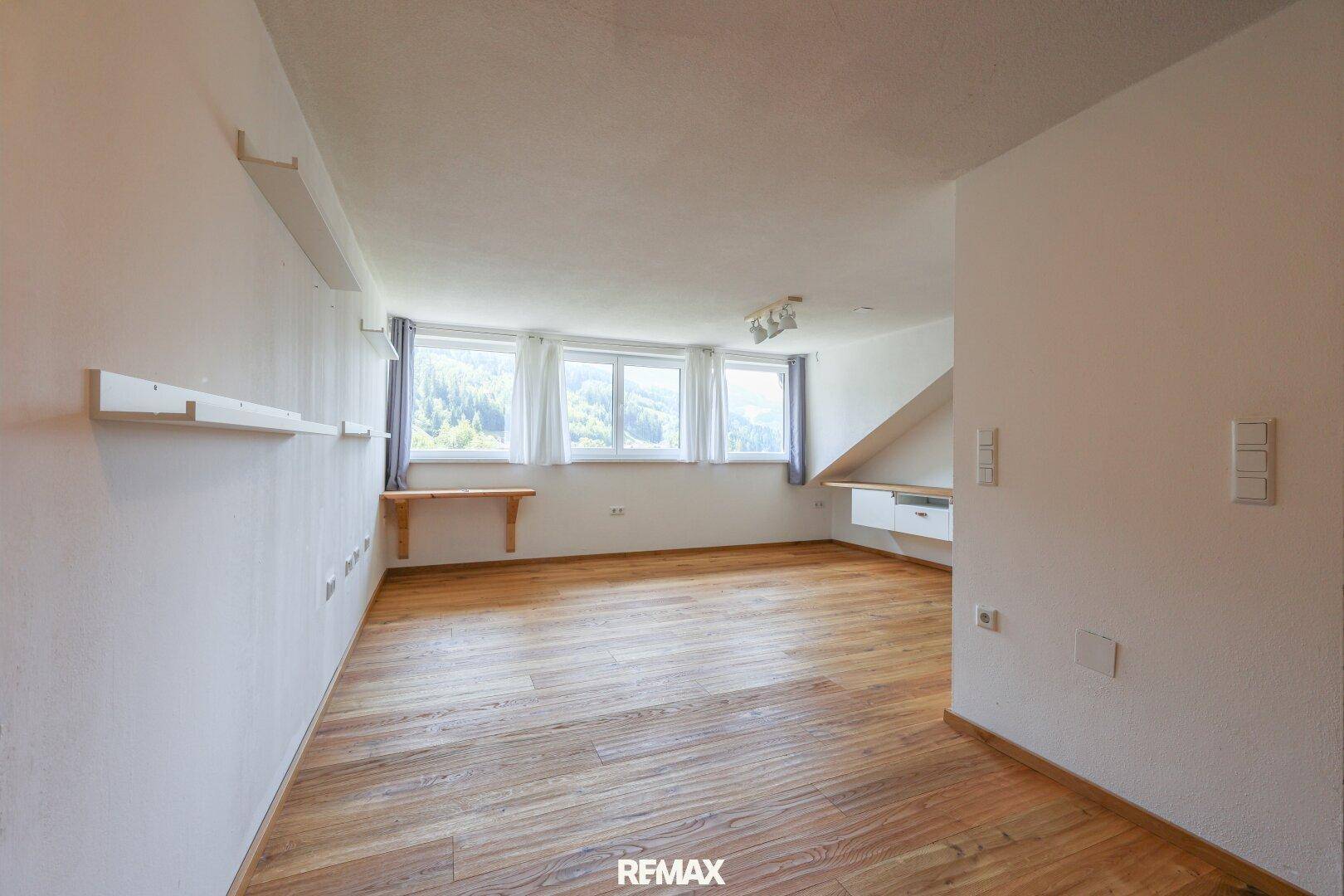 Großes, helles Wohnzimmer mit Holzboden und mehreren Fenstern mit Bergblick.