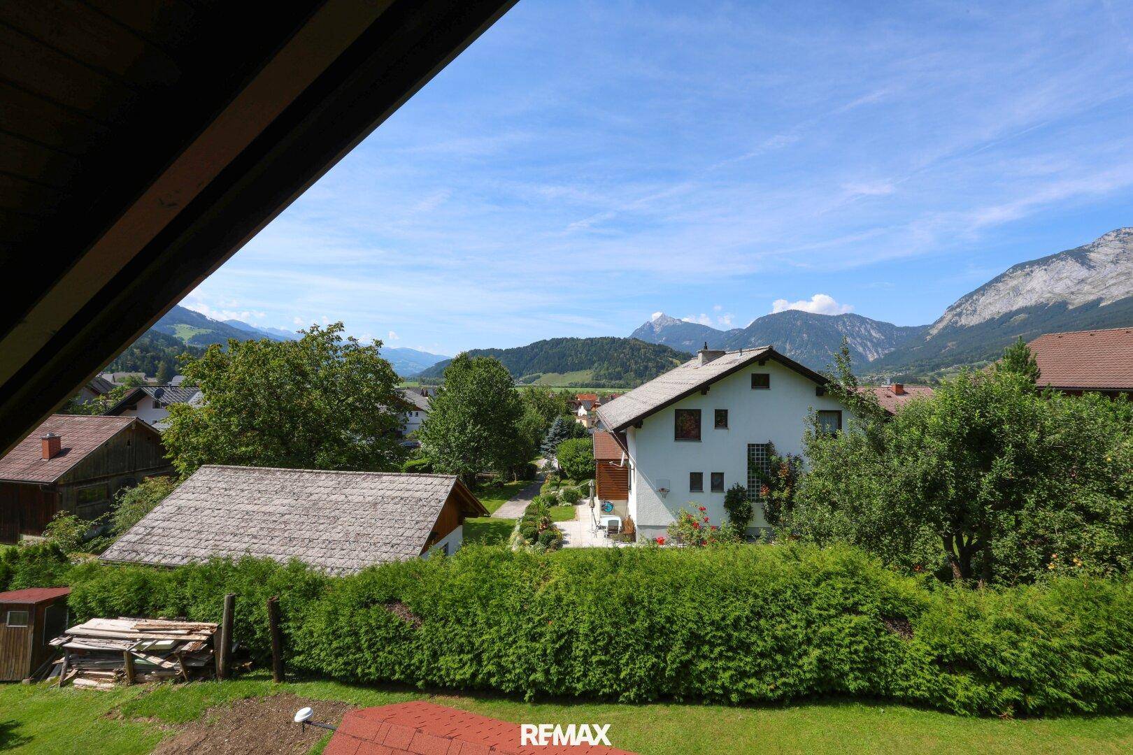 Panoramablick auf die ländliche Umgebung mit Häusern und Bergen unter blauem Himmel.