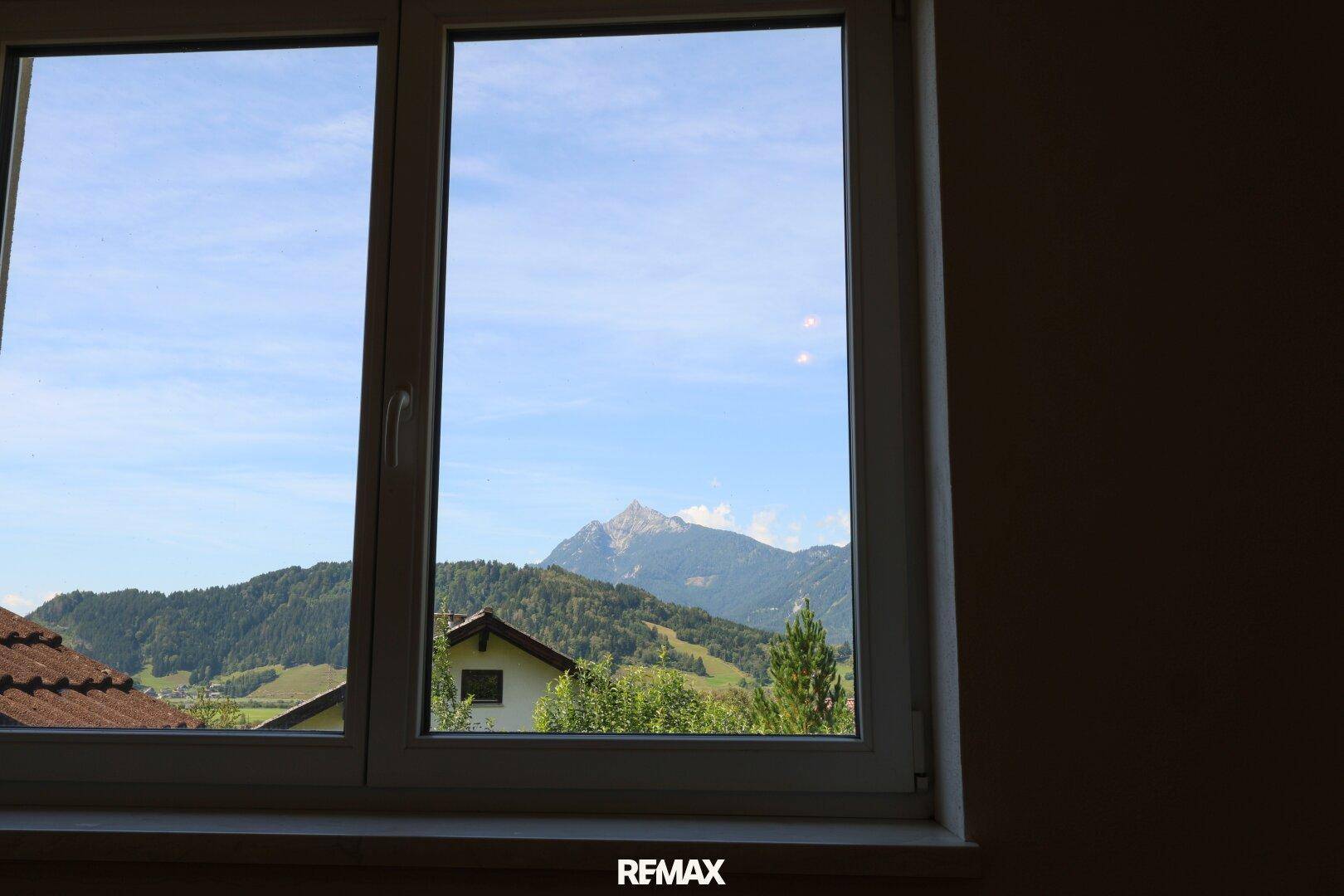 Fensterblick auf die malerische Berglandschaft und grüne Hügel unter klarem Himmel.
