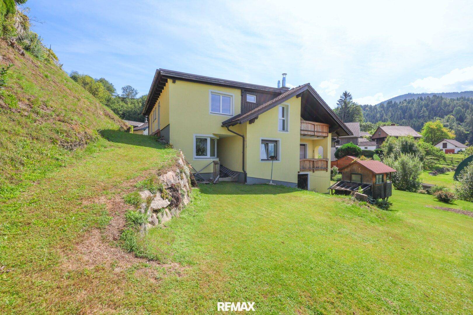 Großzügiger Gartenbereich mit Rasenfläche und einem gelben Haus am Hang.