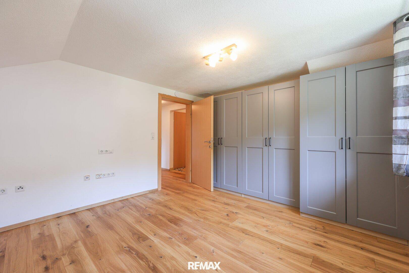 Geräumiges Schlafzimmer mit Holzboden und modernen grauen Einbauschränken.