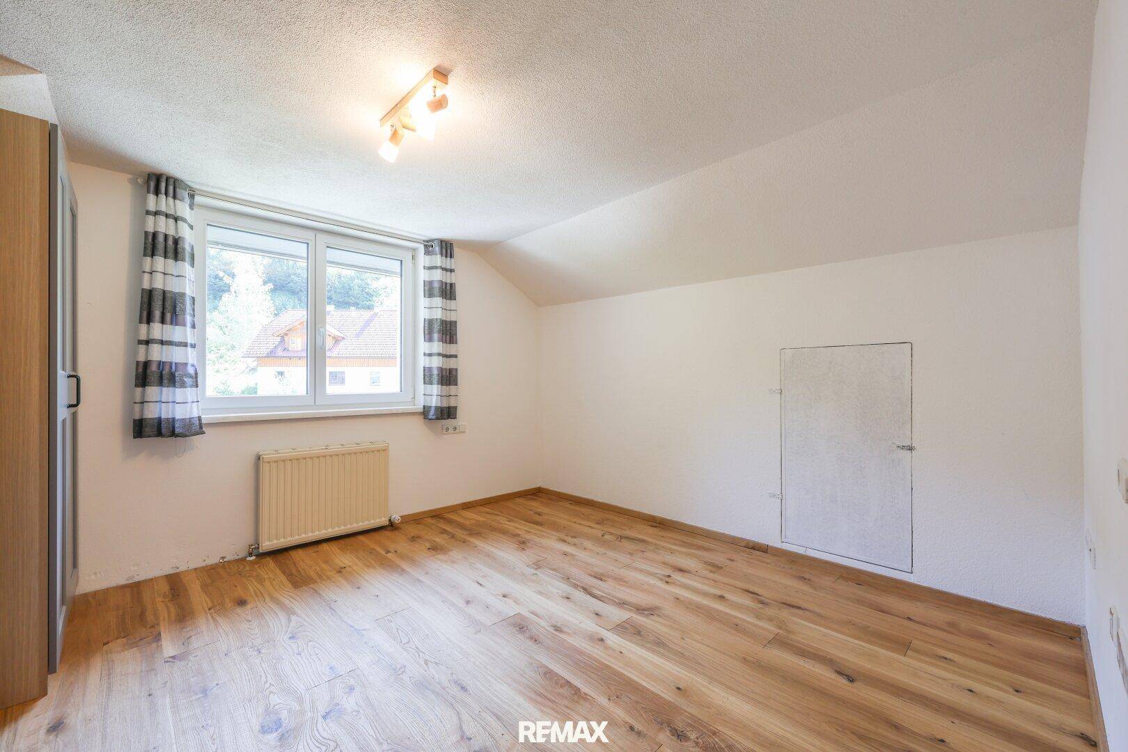 Helles Zimmer mit Holzboden, Fenster und Heizkörper, ideal als Schlaf- oder Kinderzimmer.